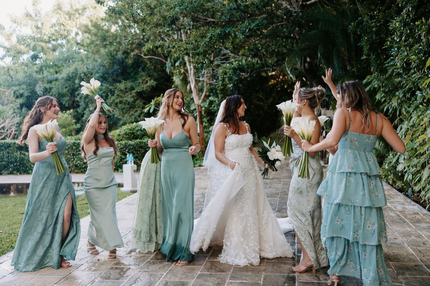Wedding party in seafoam dresses walking and posing playfully on stone pathway.