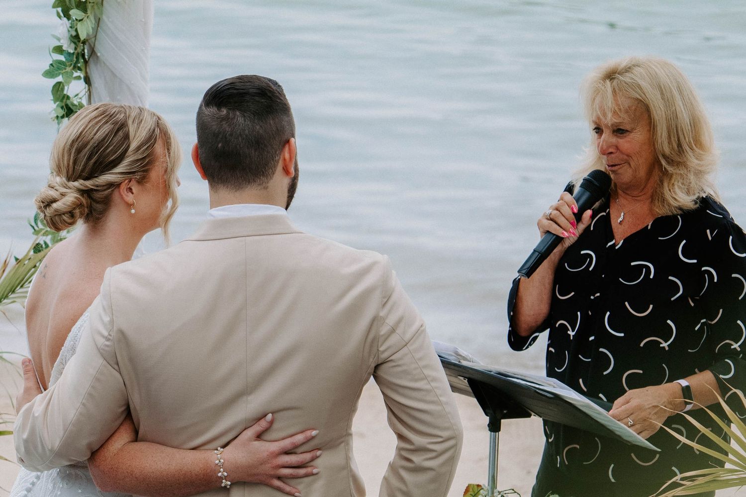 Emotional wedding ceremony moment captured on a beachfront deck with floral decorations.