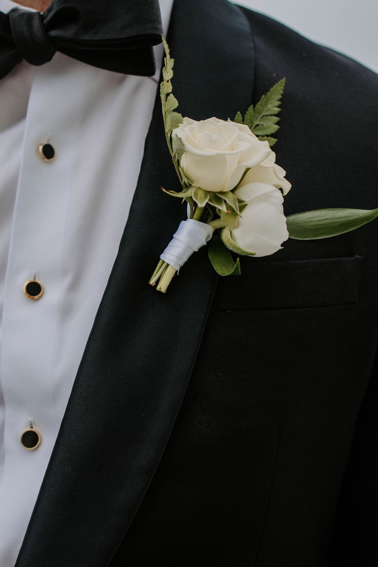 Close-up details of white rose boutonnieres on black tuxedo lapels.