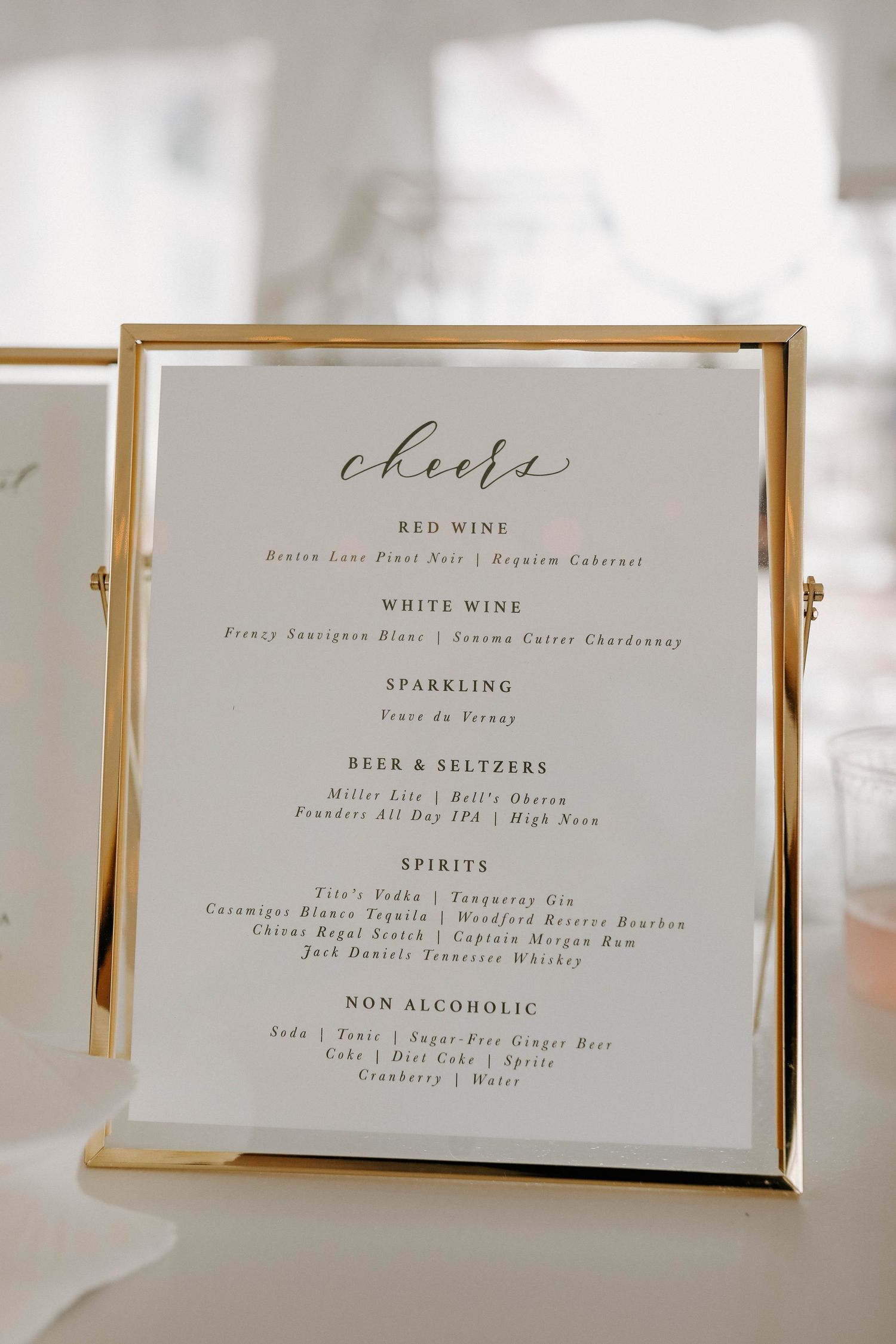 Wedding drink menu cards in gold frames showing wine, beer and cocktail selections.
