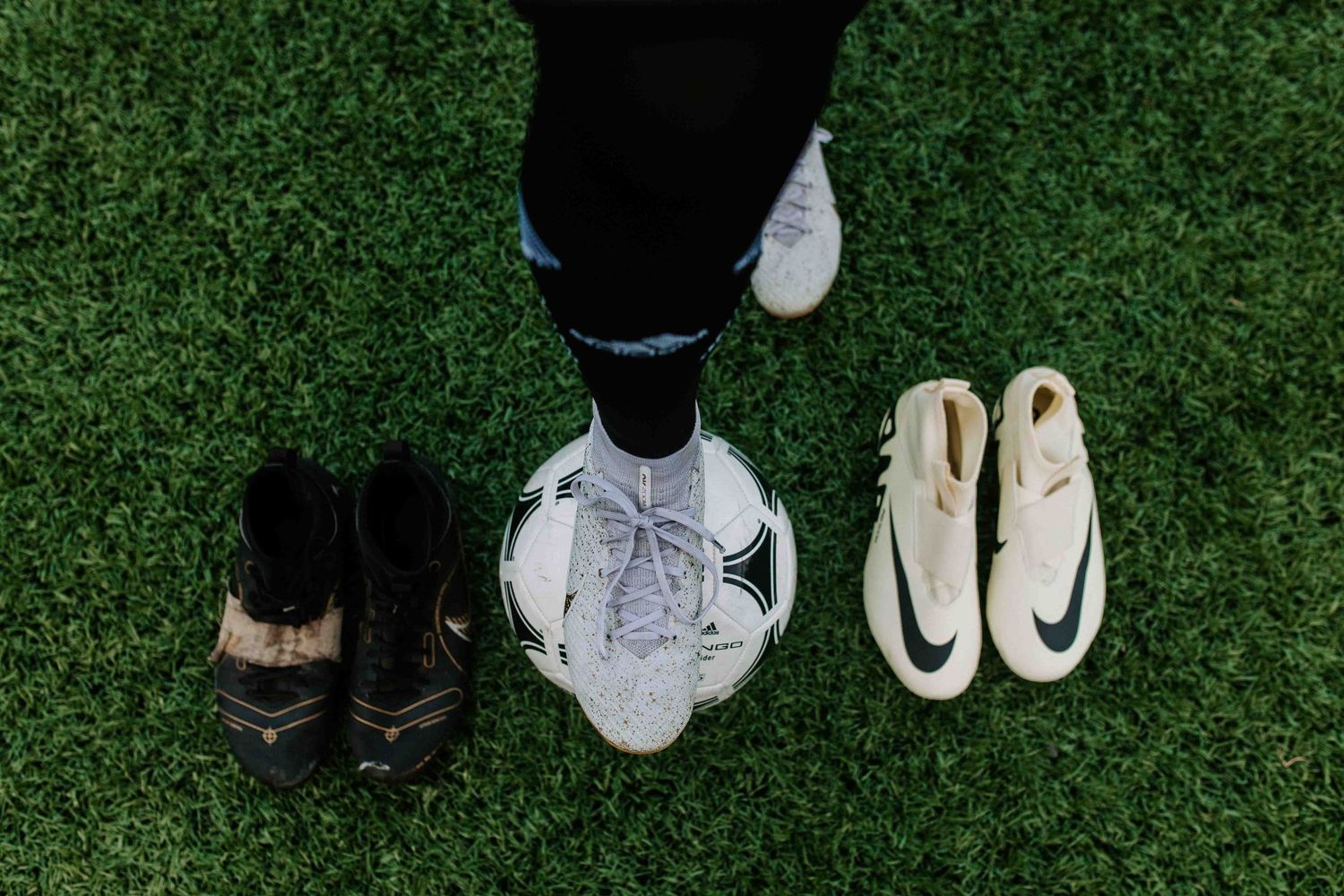 Various soccer cleats and balls displayed on artificial turf.
