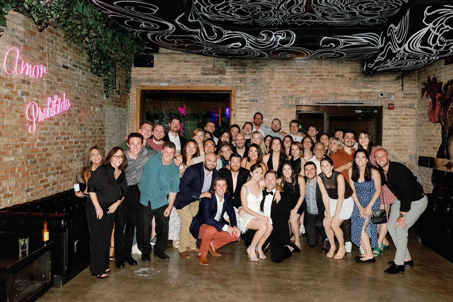 Large group photo of wedding guests posed against a brick wall.