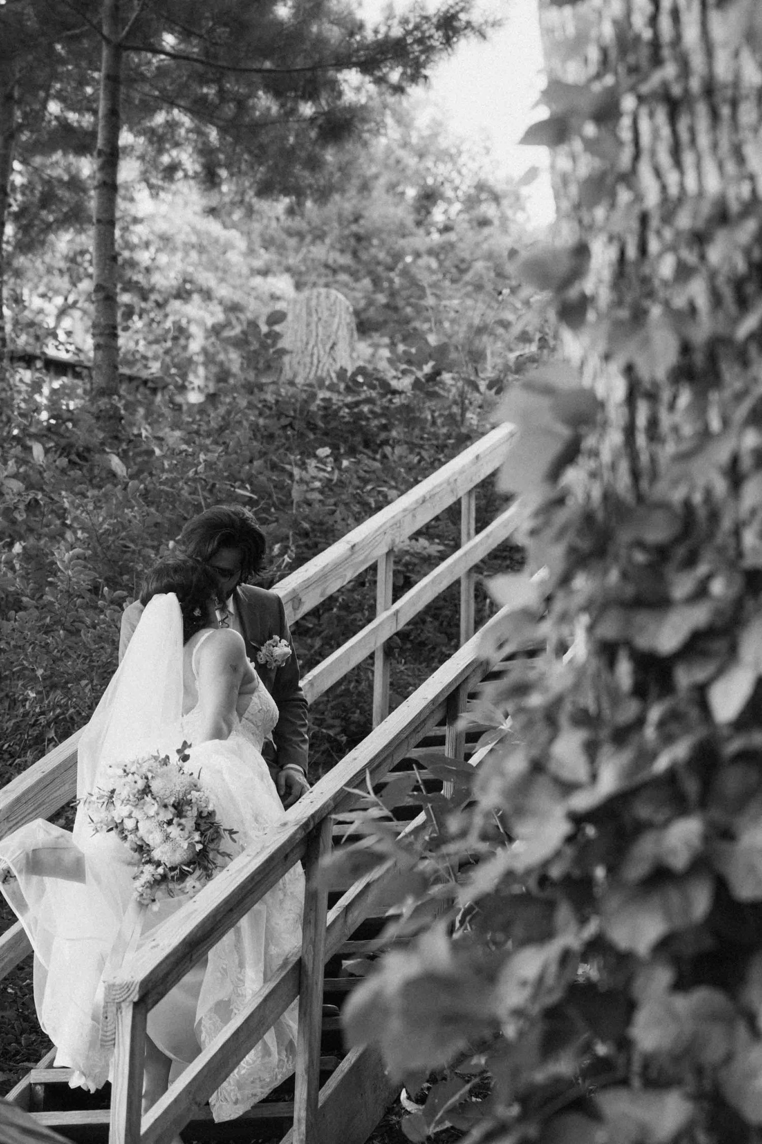 Black and white wedding photos captured on wooden stairs surrounded by foliage.