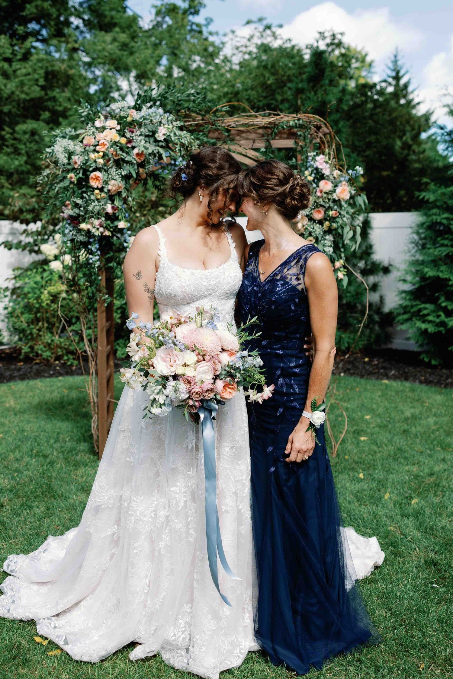 Wedding detail shot showing white lace dress and navy blue bridesmaid gown with floral bouquets.