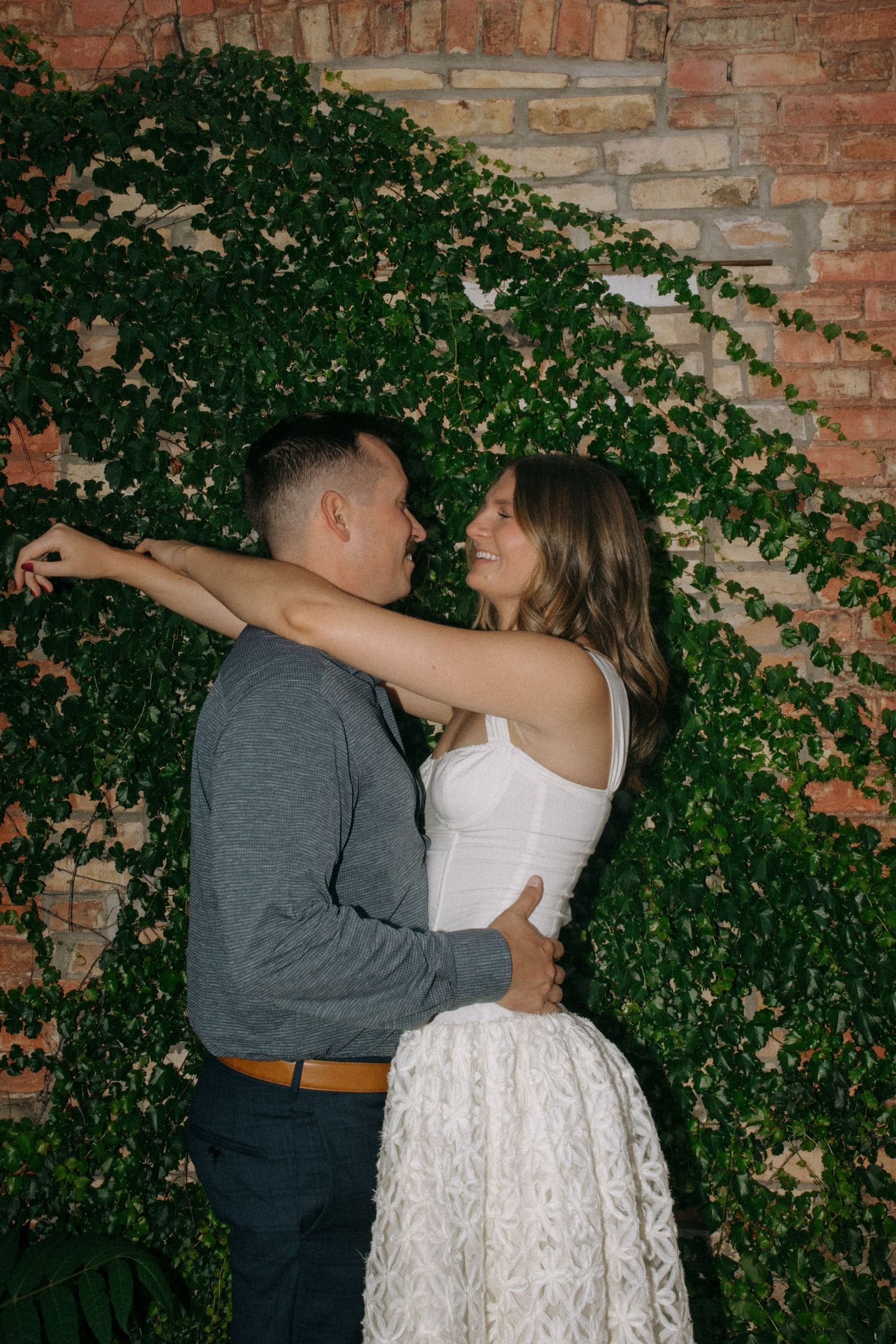 A couple sharing intimate moments against an ivy-covered brick wall.