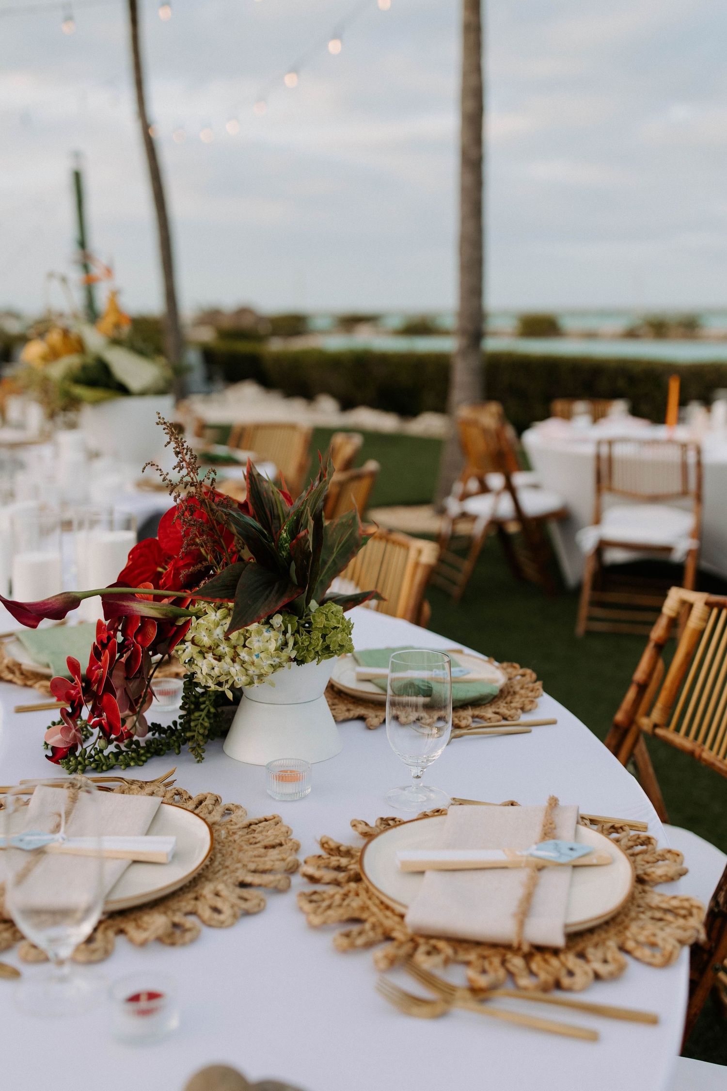 Elegant table setting with red floral centerpiece and gold charger plates at outdoor reception.