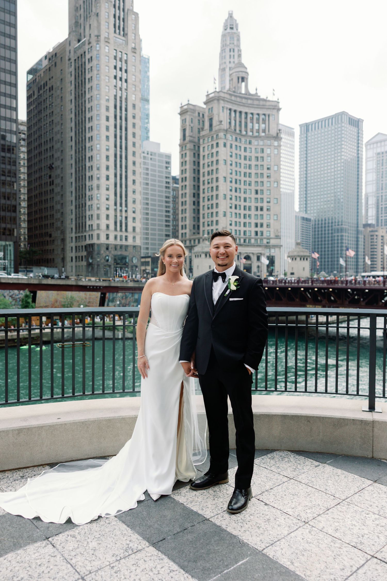 Wedding couple posing along Chicago River with iconic architecture in background.