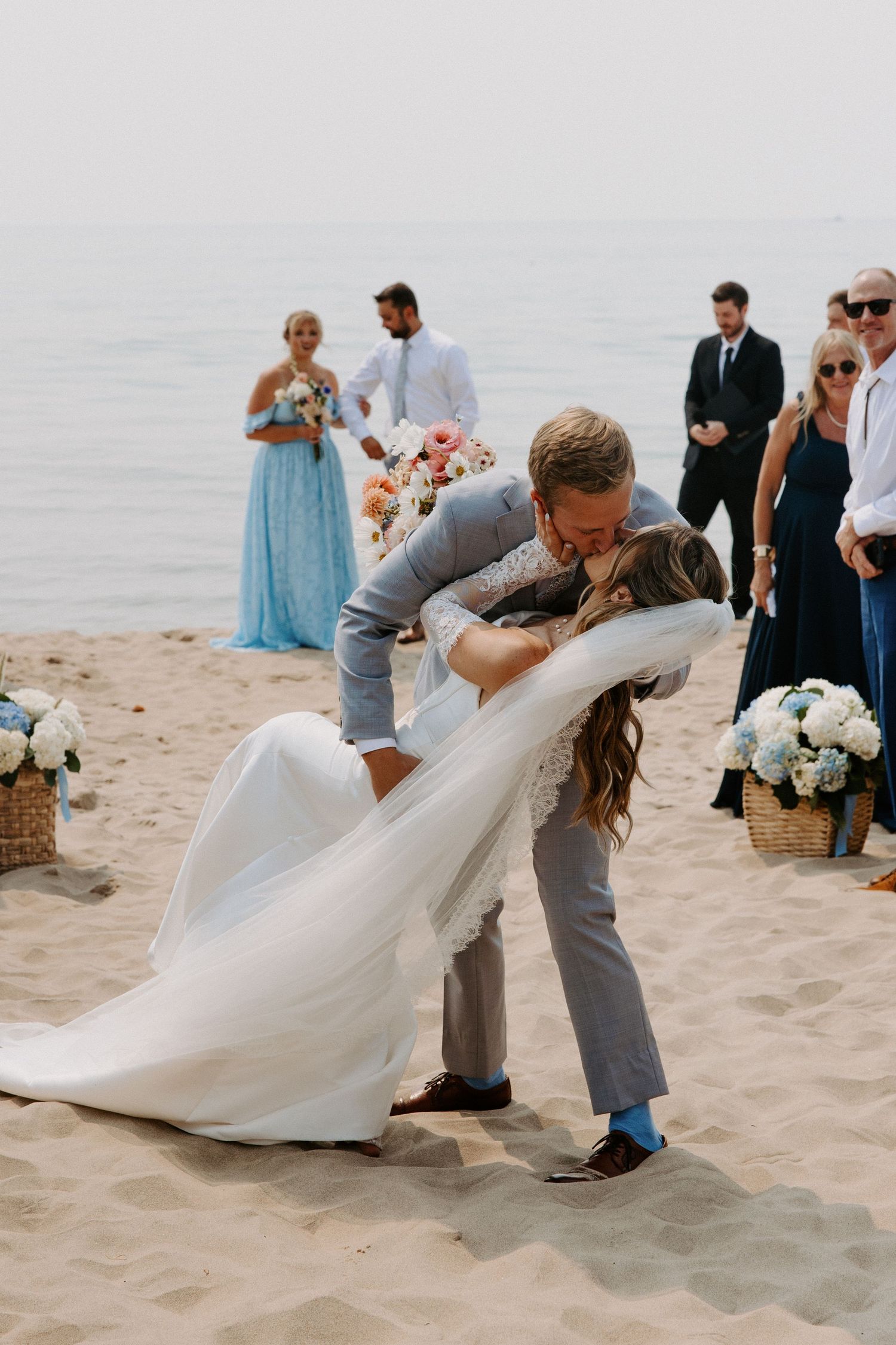 Newlyweds share romantic dips and kisses on a sandy beach.