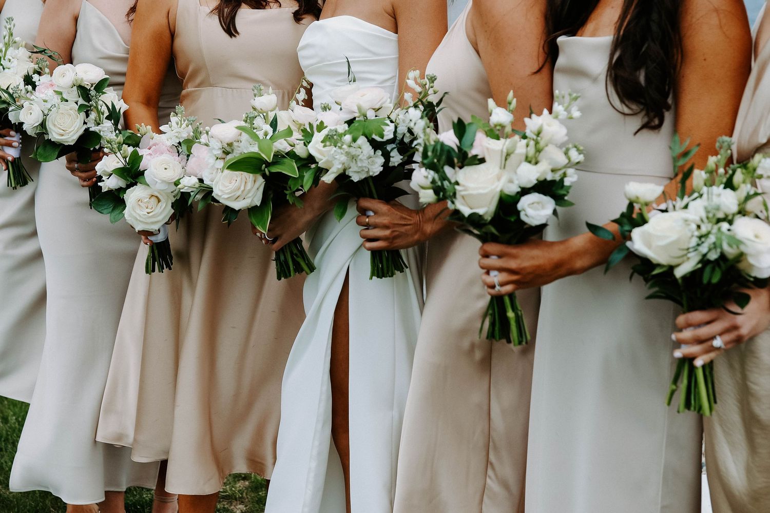 Bridesmaids in neutral dresses holding elegant white and green floral bouquets.