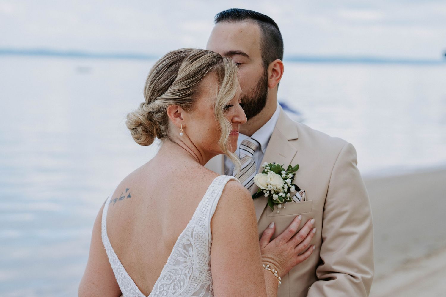 A romantic wedding couple shares an intimate kiss on a beach with ocean waves in the background.