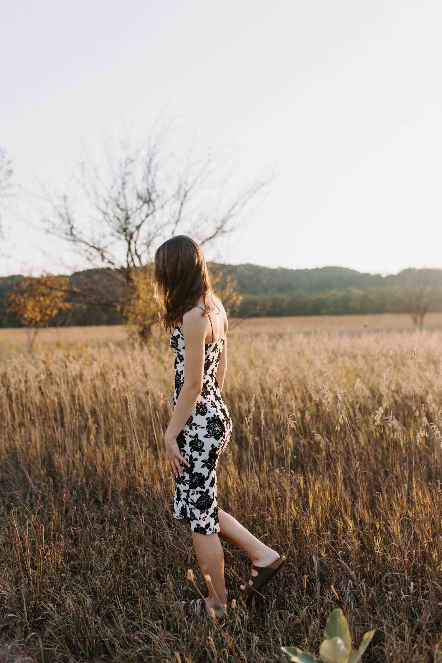 Black and white patterned dress contrasts with tall golden grass in a sunset meadow.