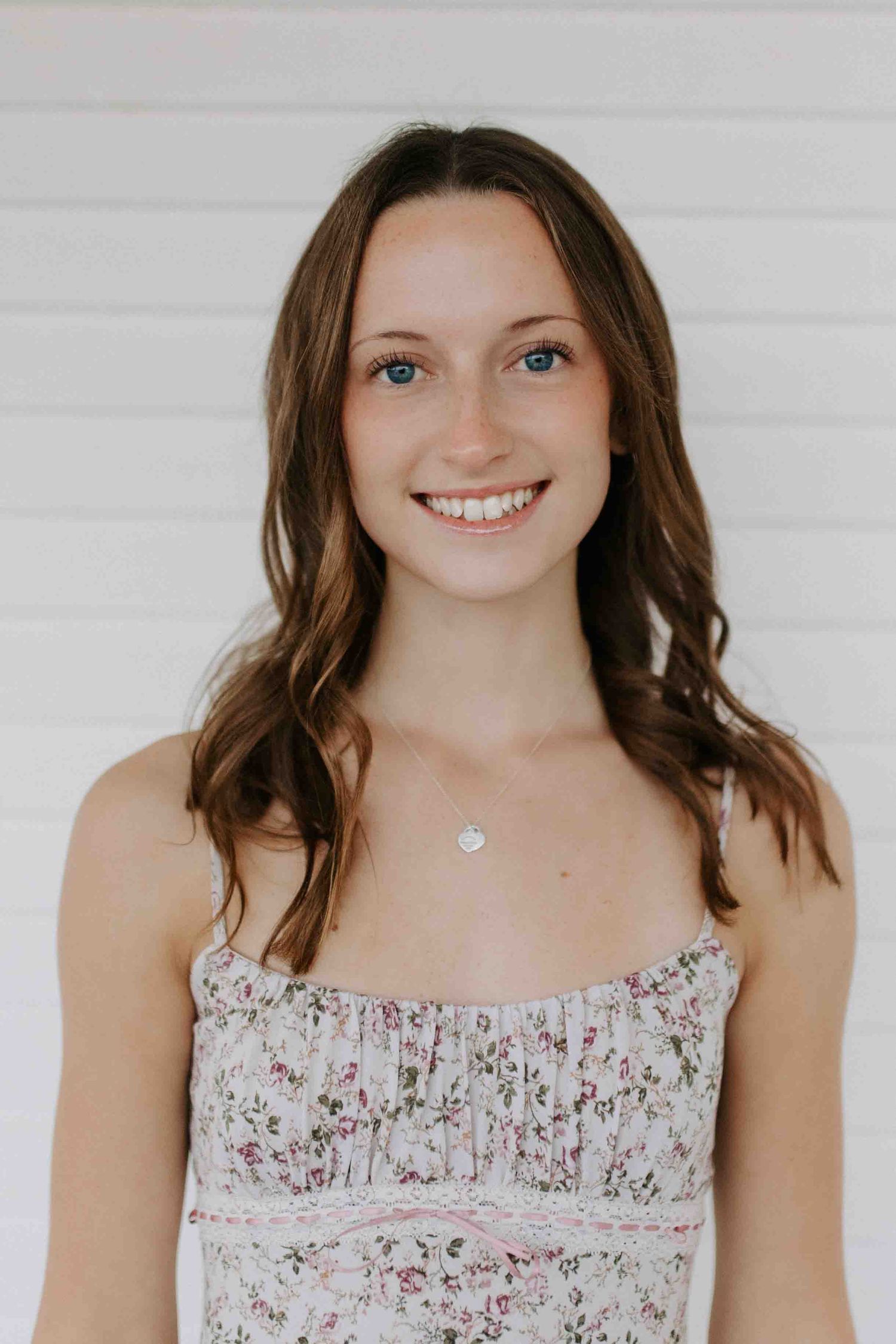 Portrait against a white backdrop showing a floral sundress and delicate necklace.