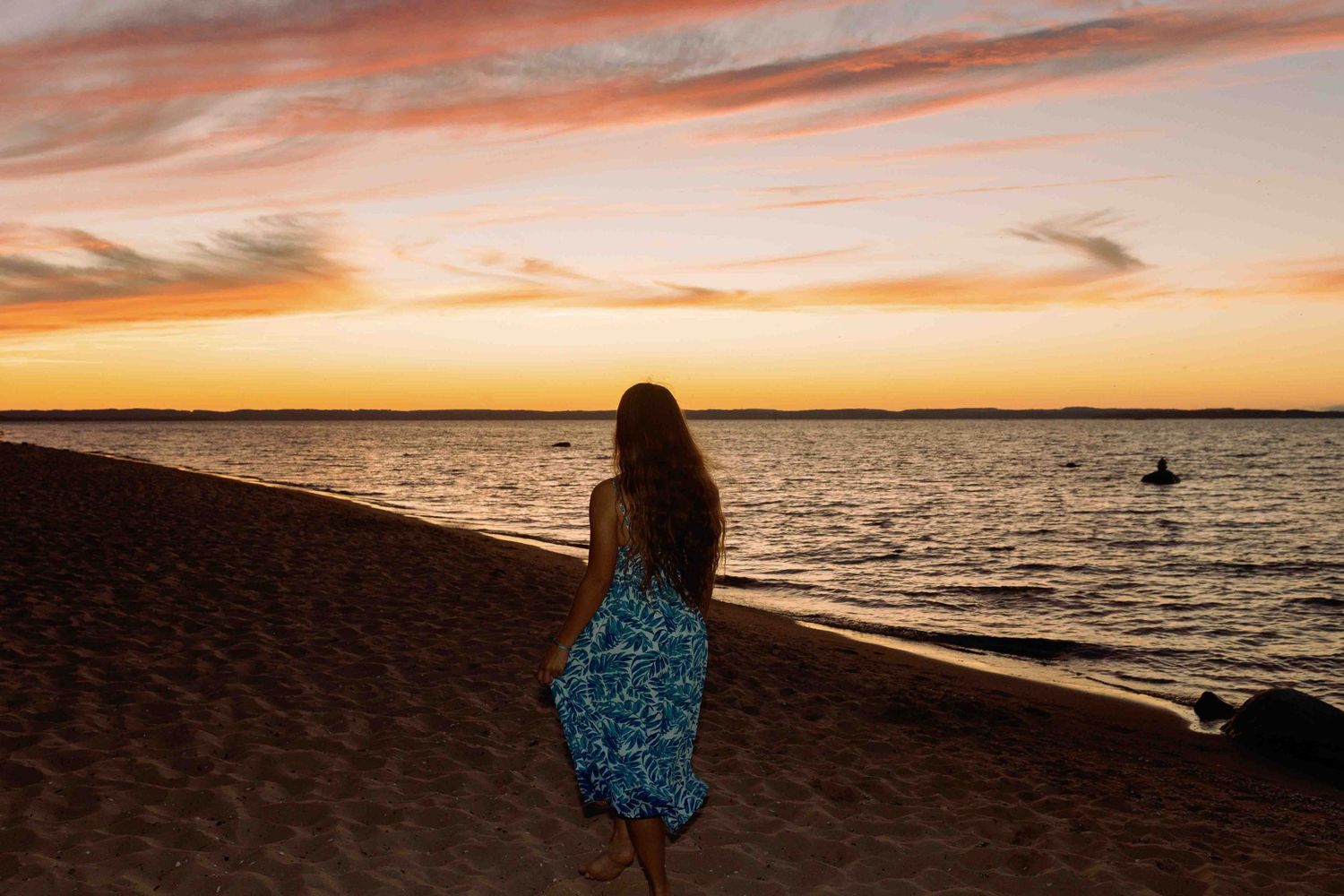 Scenic coastal view with dark silhouettes against an orange and pink sunset sky.