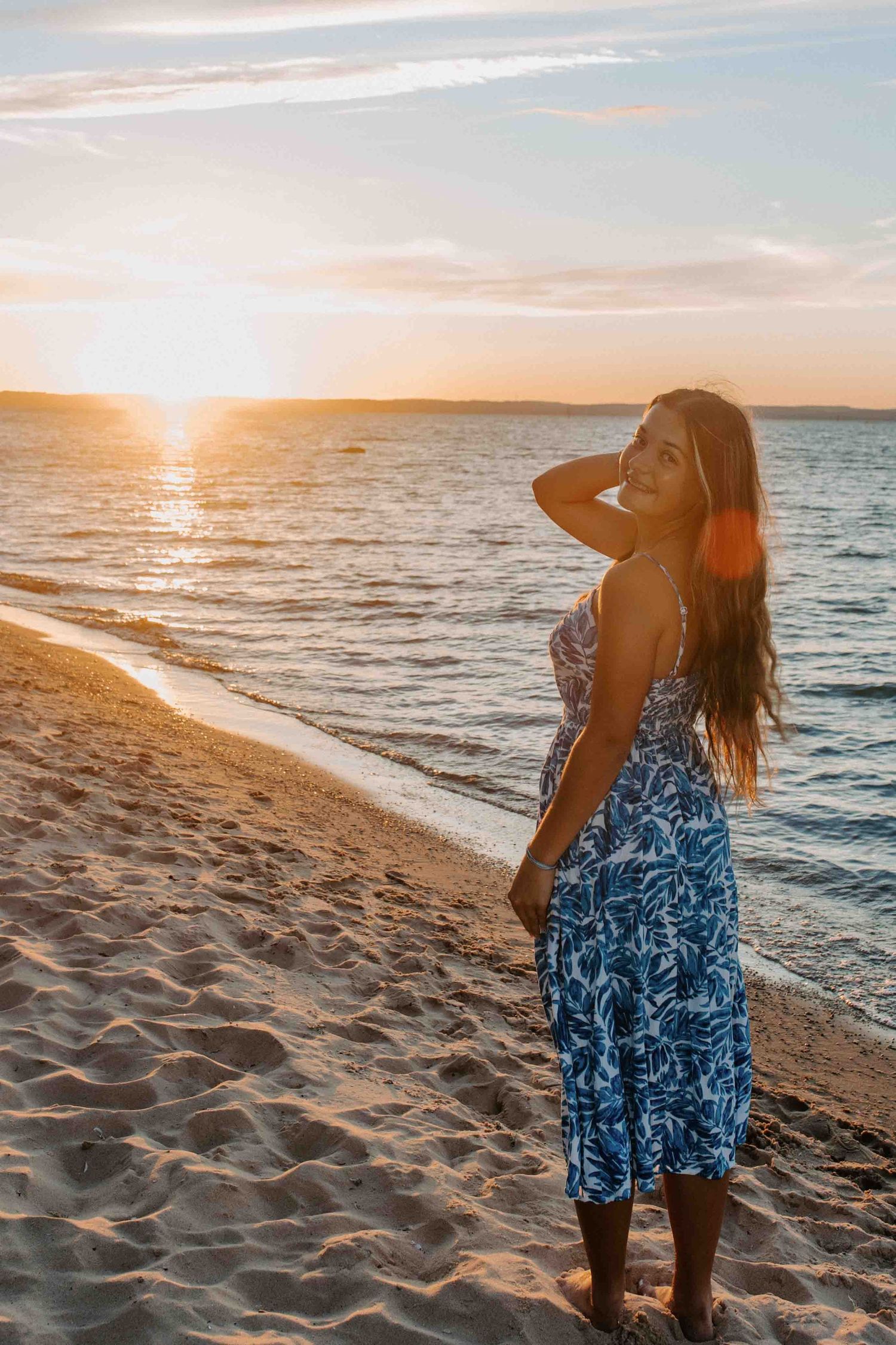 Person in blue patterned dress poses on beach during golden hour.