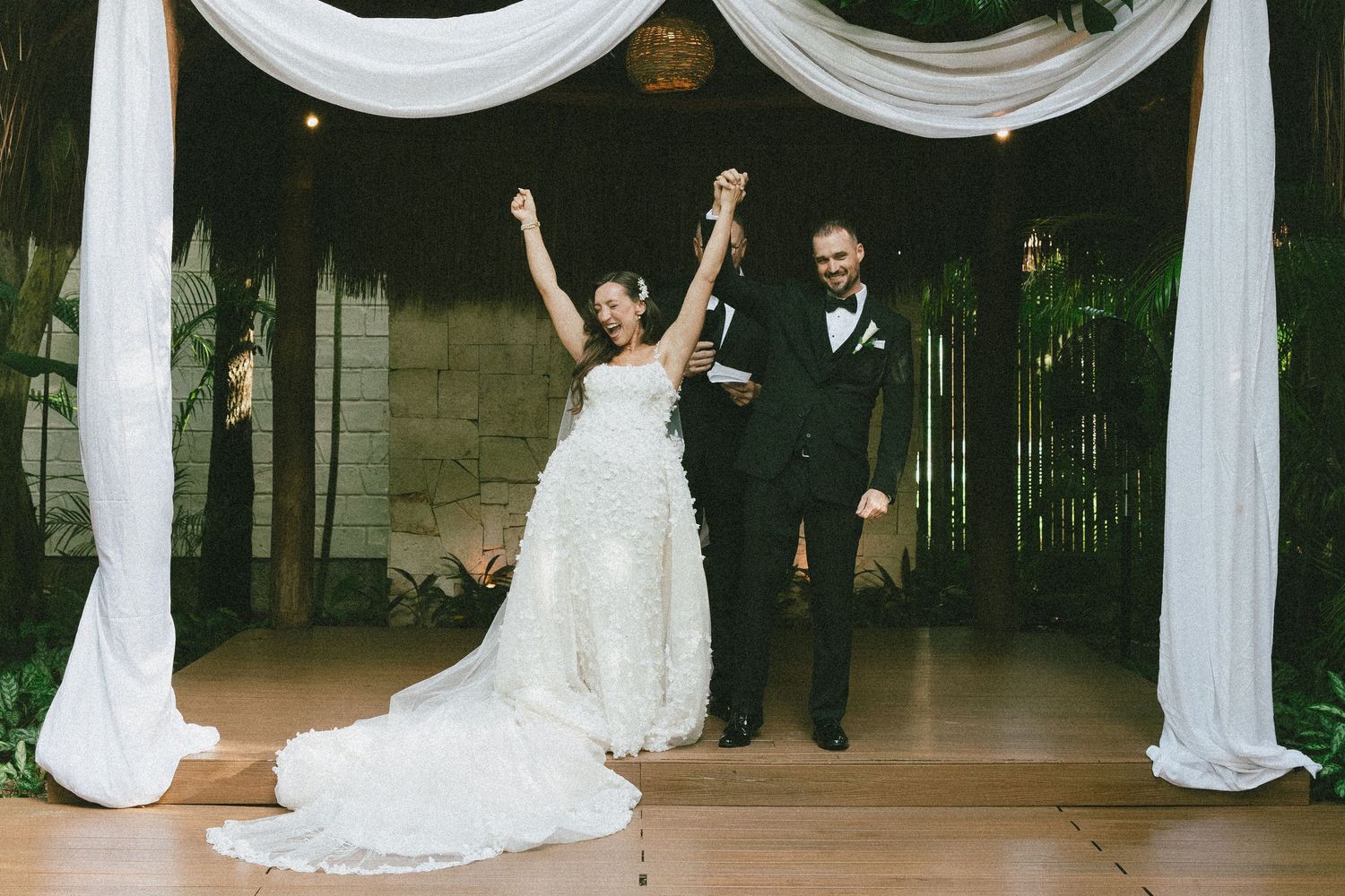 Wedding couple performing celebratory dance moves under elegant white draping and floral decor.