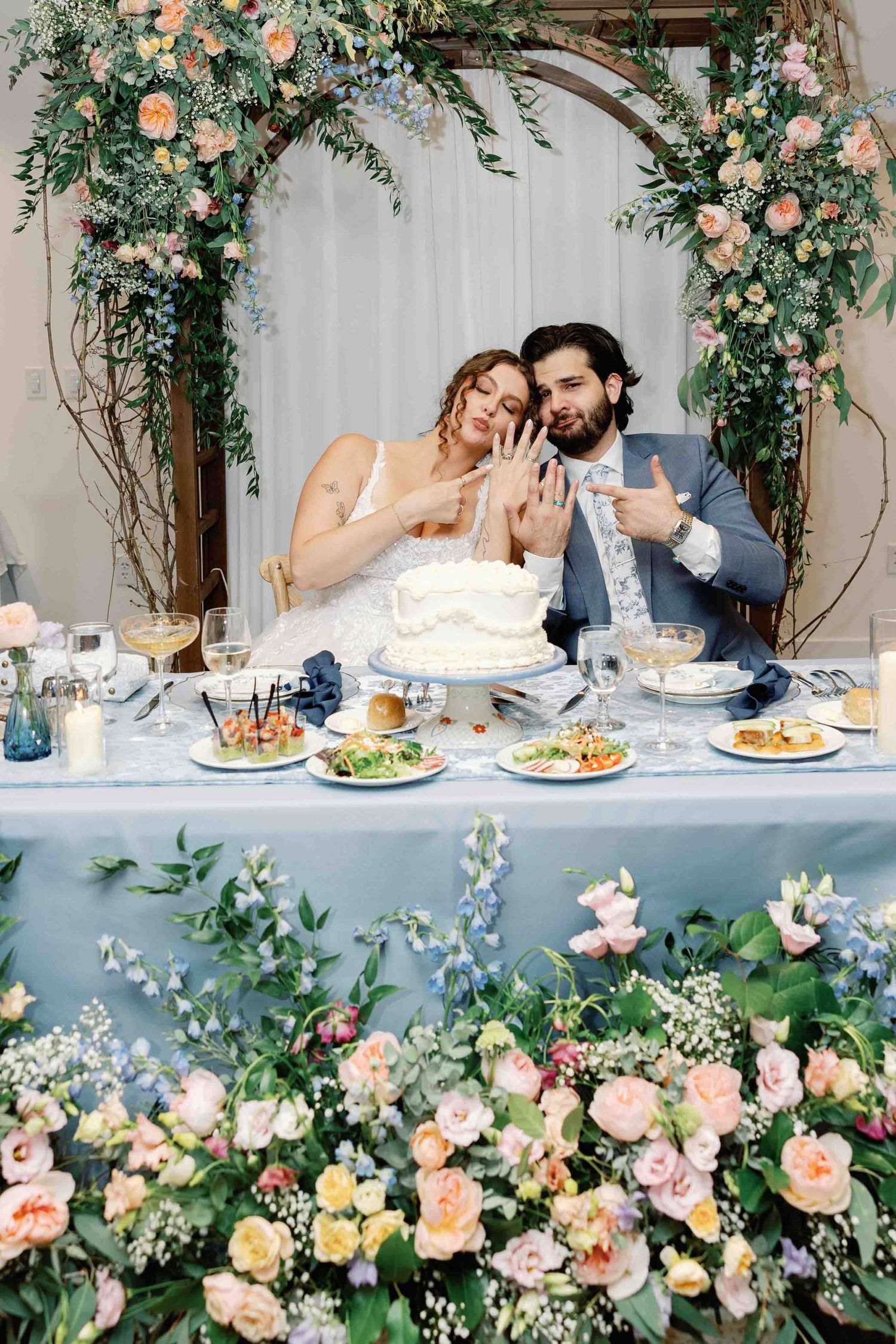 Newlyweds seated at a floral-decorated head table share intimate moments during their reception.