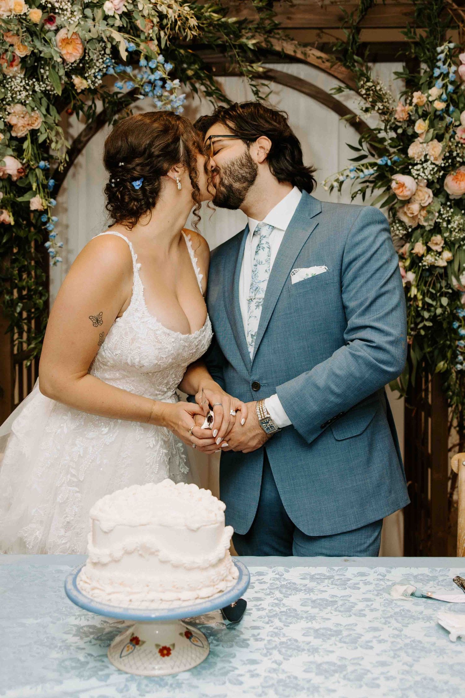 Wedding couple sharing cake-cutting moments under floral arch decorations.