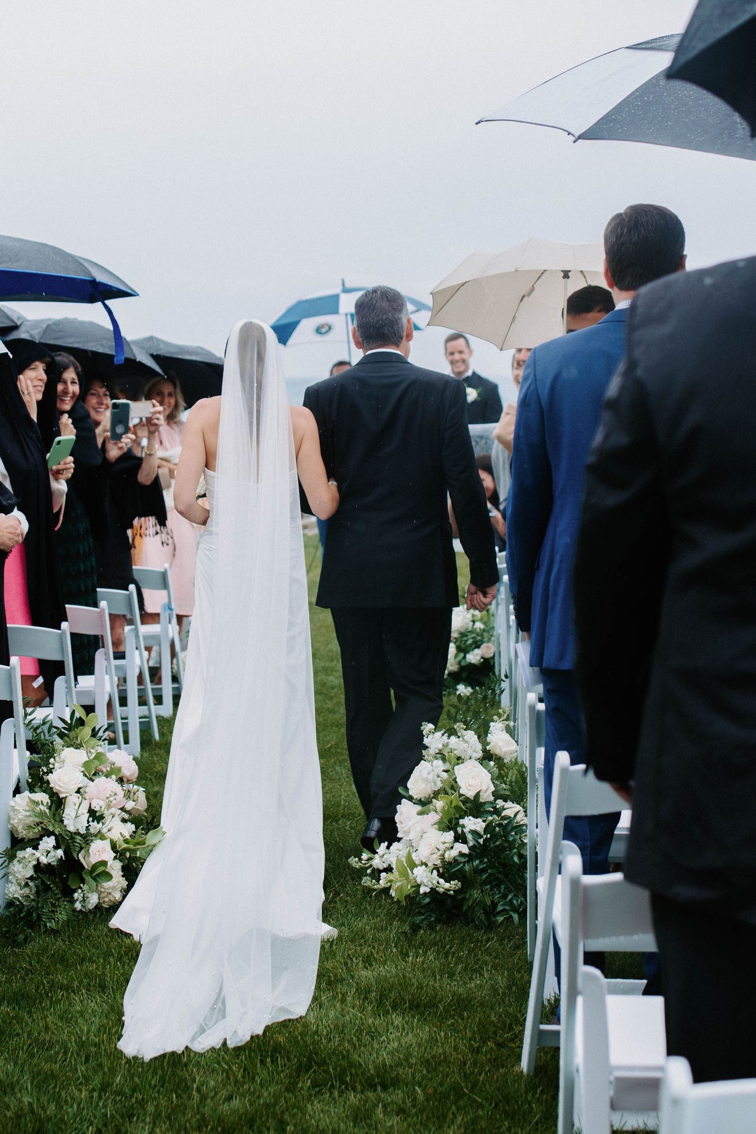 Wedding ceremony setup with white chairs and floral arrangements during light rain.