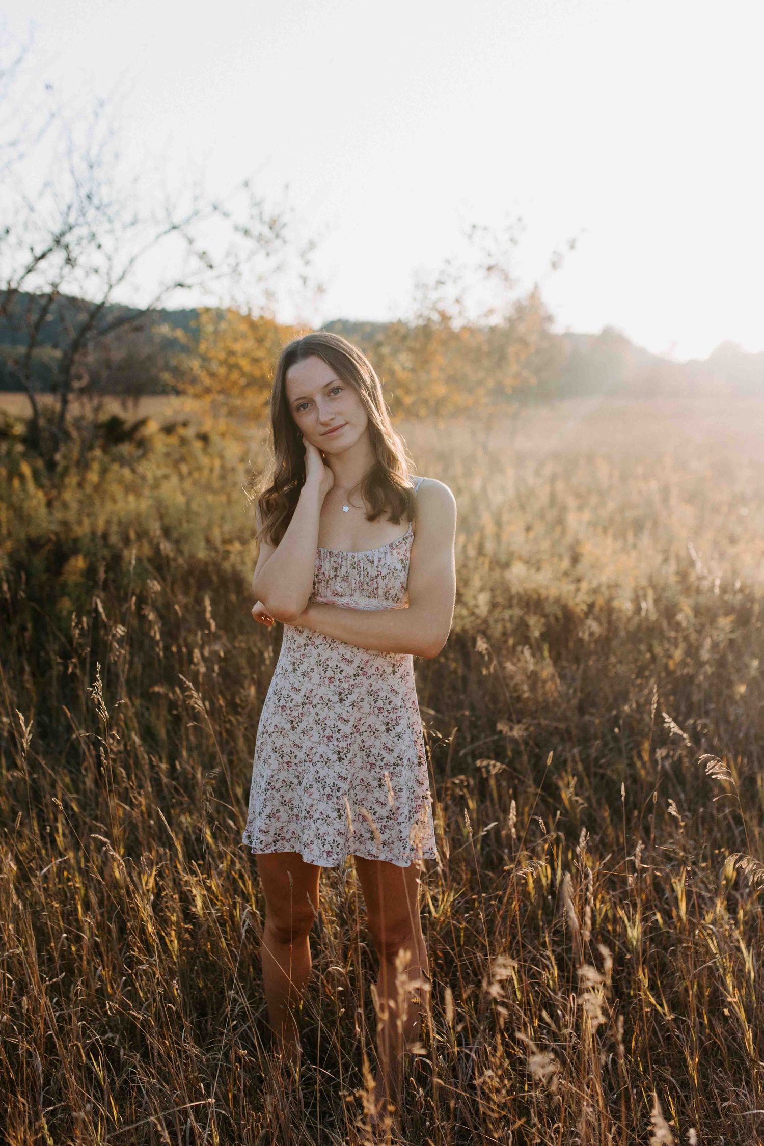 Candid shot of someone in a white floral dress standing among tall autumn grasses.