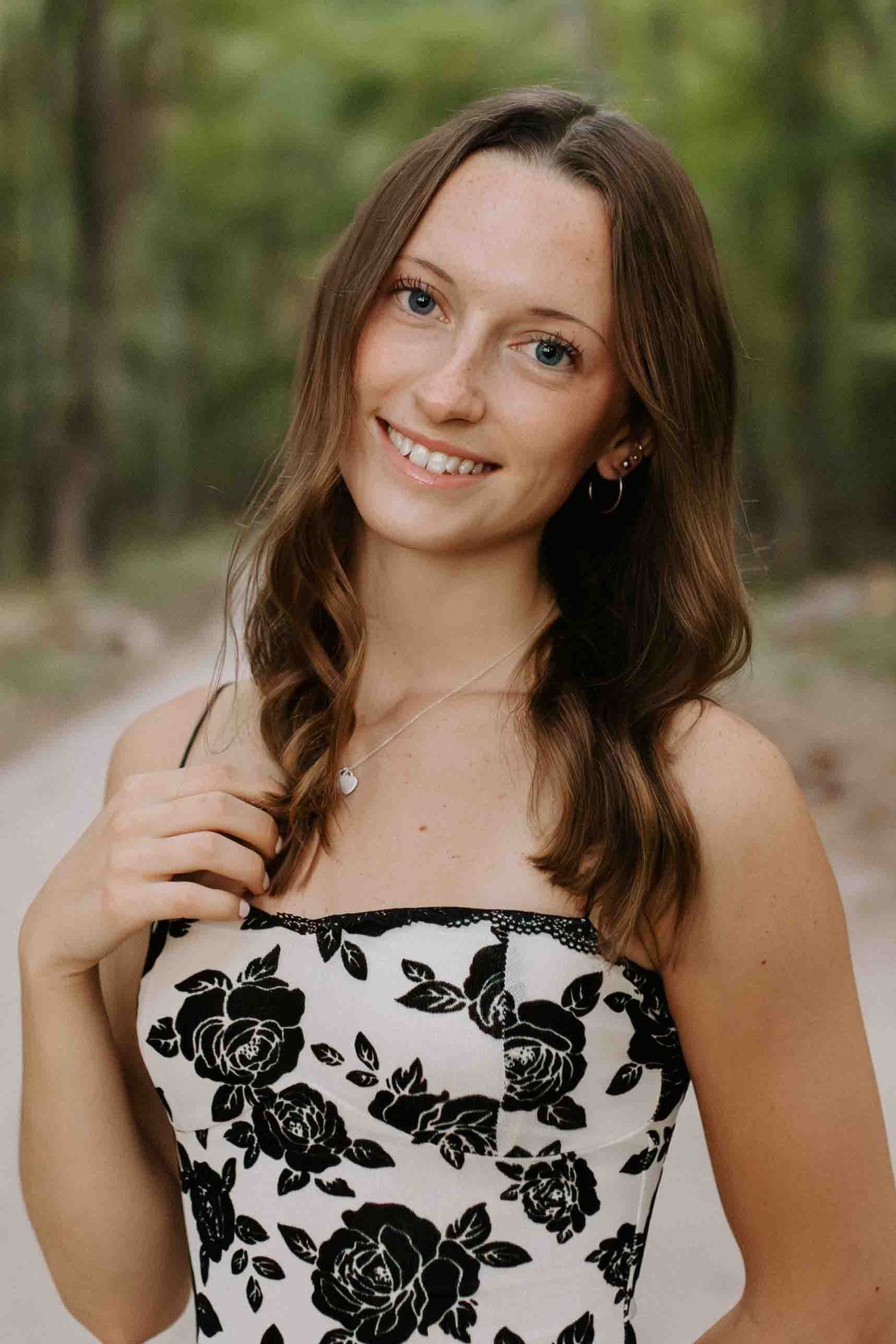 Outdoor portrait in a white dress with black floral pattern surrounded by lush greenery.