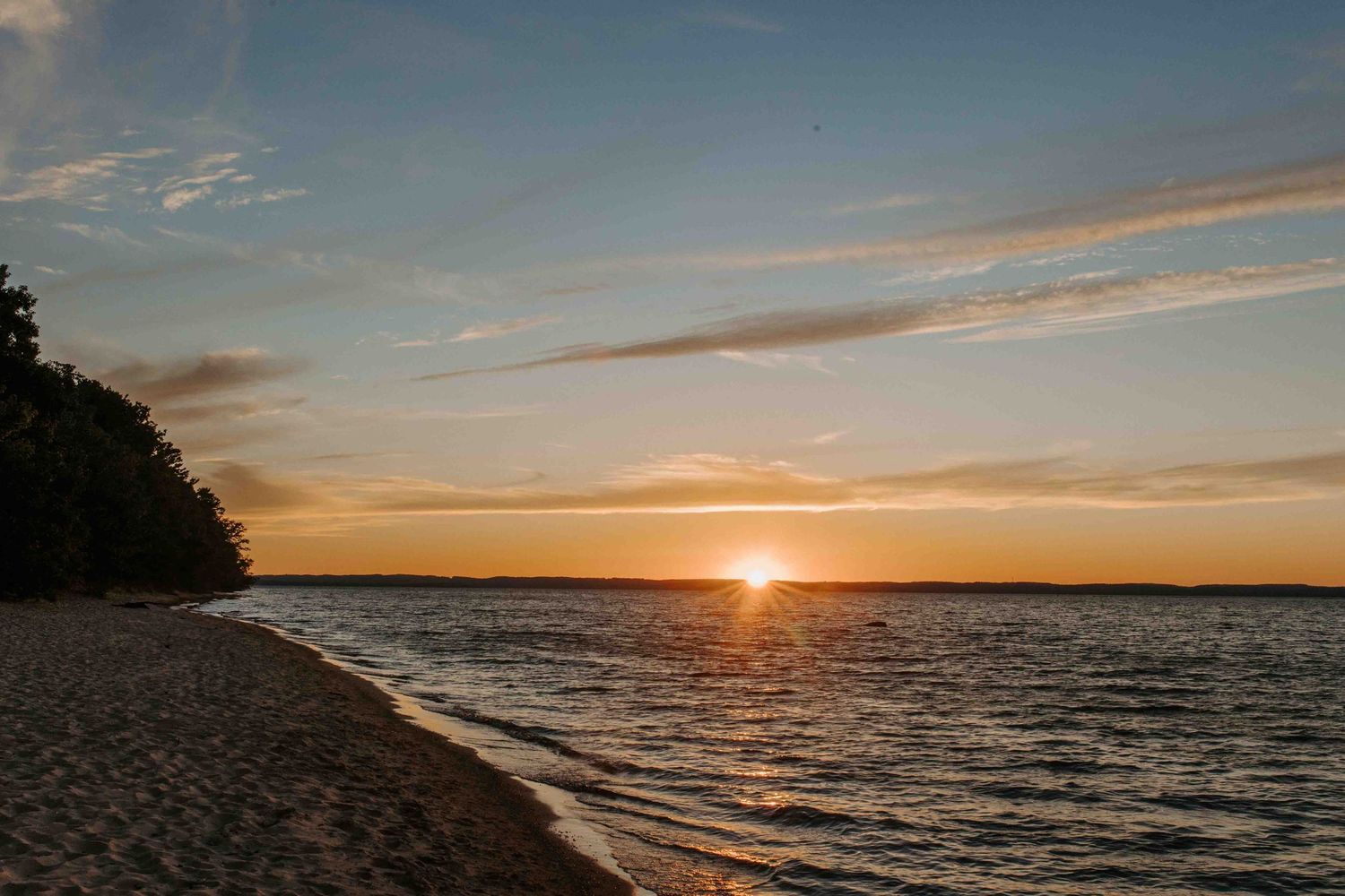 Panoramic sunset view over calm ocean waters with orange sky and clouds.