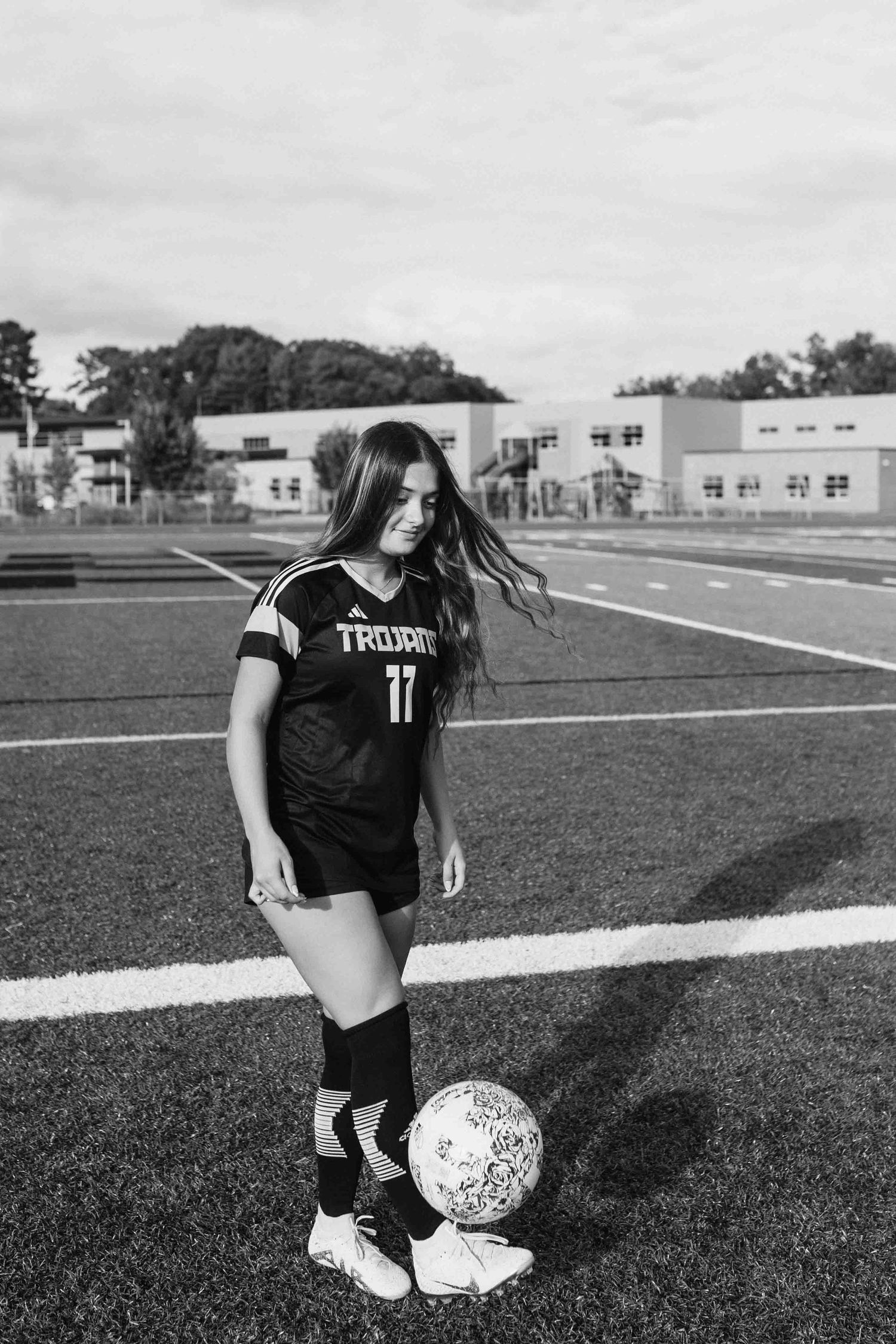 Black and white portrait of soccer player with ball on field in Trojans uniform.