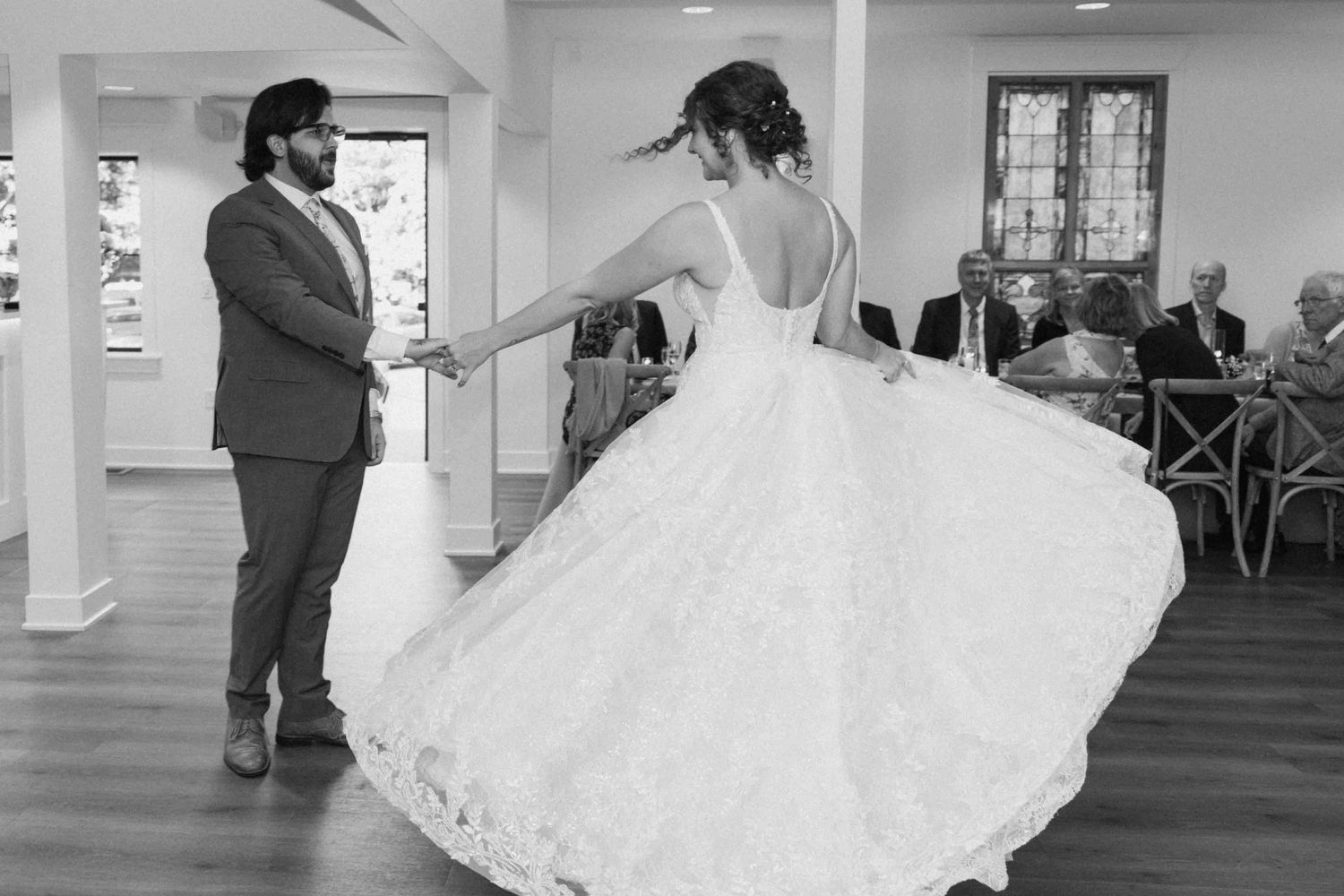 A flowing white wedding dress twirls during a dance in an indoor venue.