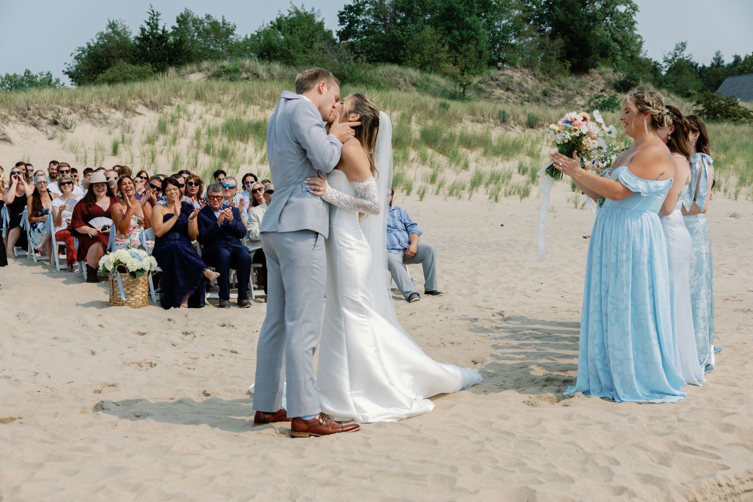Wedding party poses for photos on scenic beach with bridesmaids in light blue dresses.