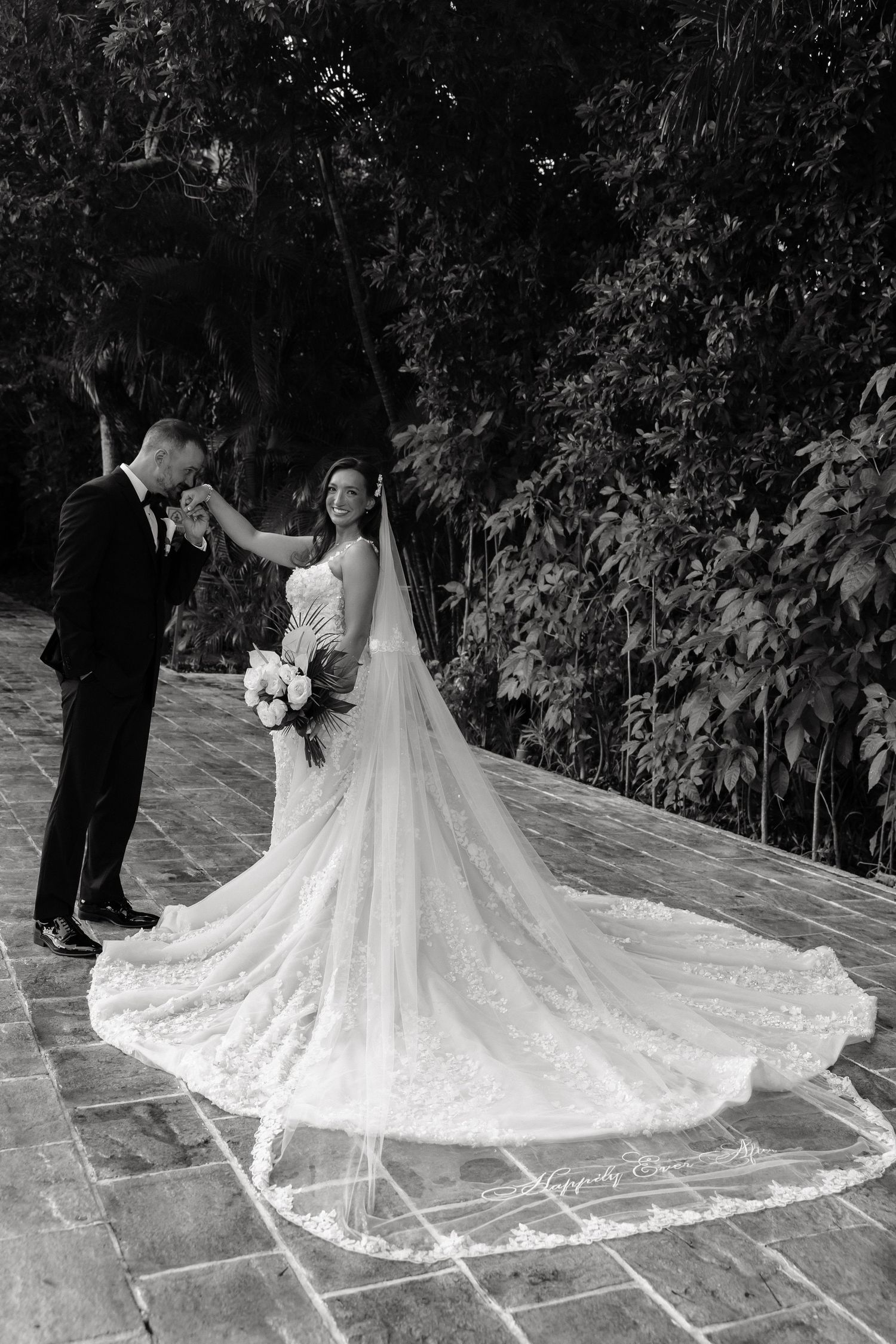 Wedding dress with intricate lace train spread out on stone patio tiles.