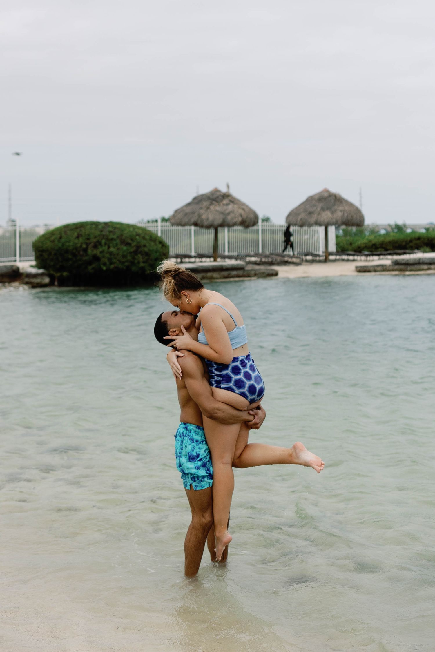 Romantic moment captured in shallow tropical waters with thatched huts in background.