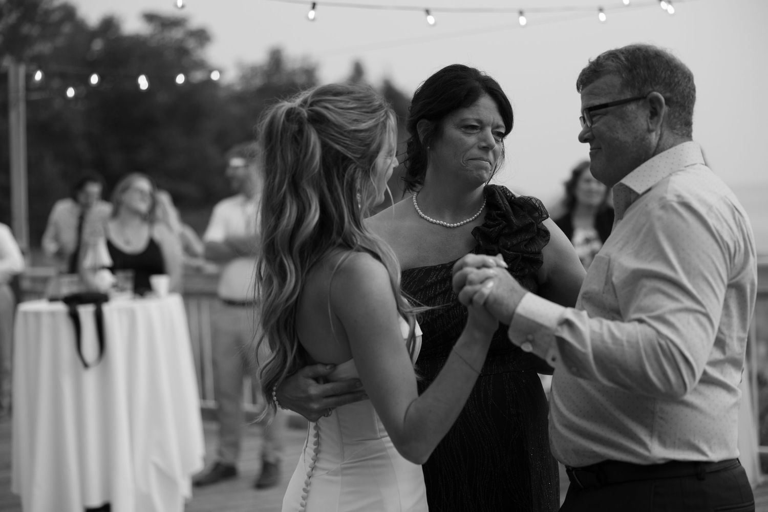 Wedding reception guests dance under string lights at an outdoor venue.