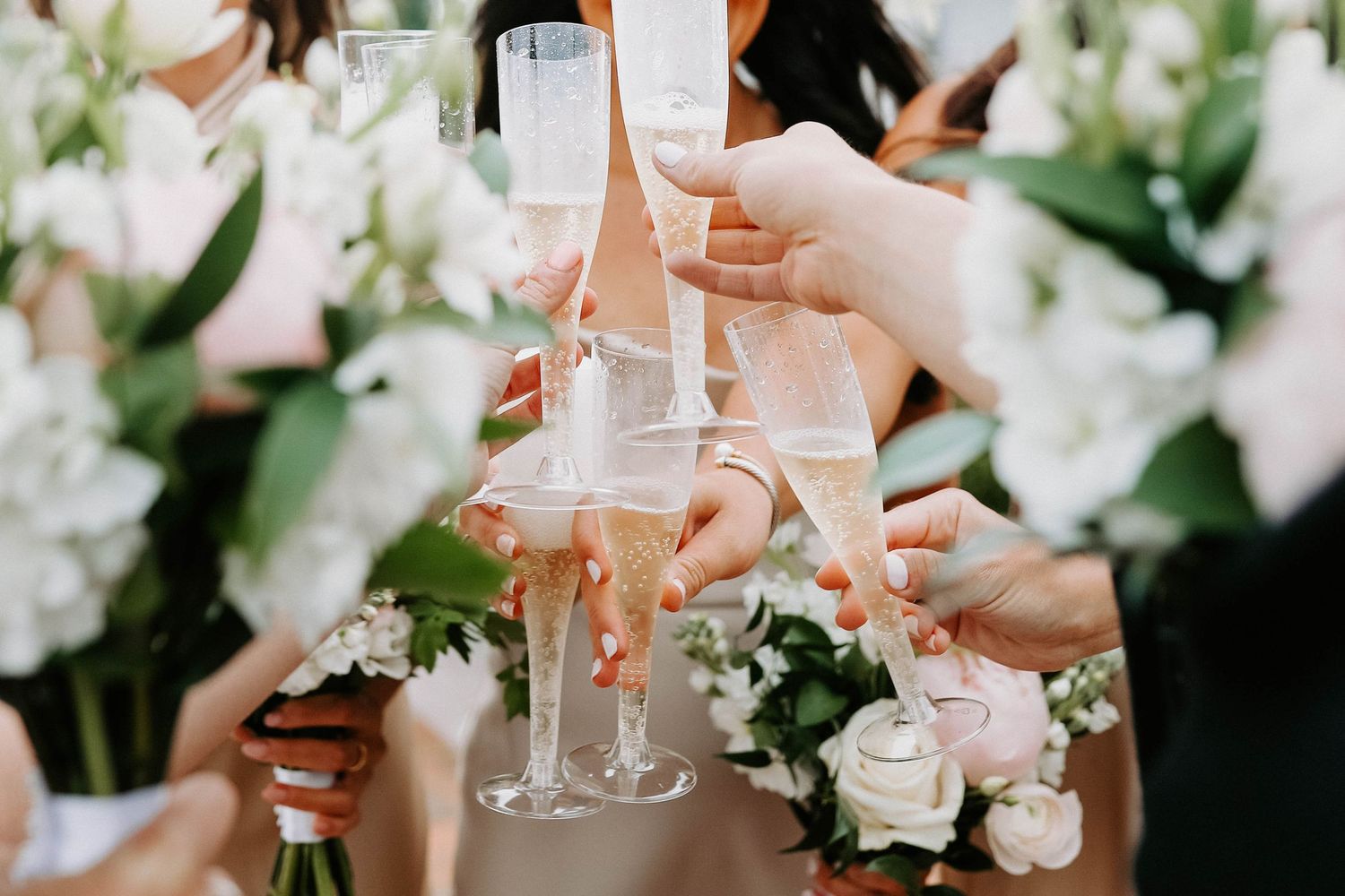 Close-up of hands toasting with champagne glasses surrounded by white flowers.