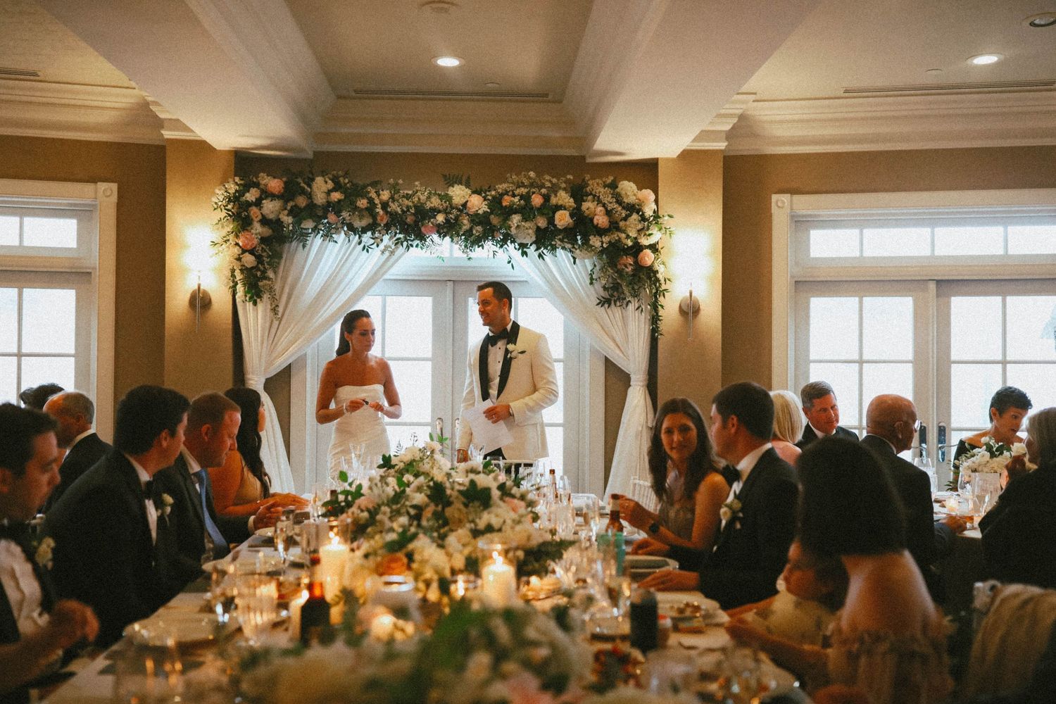 Wedding reception hall decorated with floral arrangements and warm lighting.