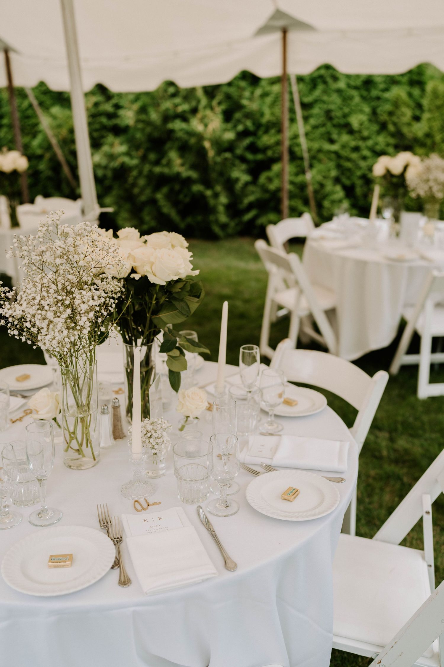 White tablescapes decorated with baby's breath and roses at an outdoor wedding reception.