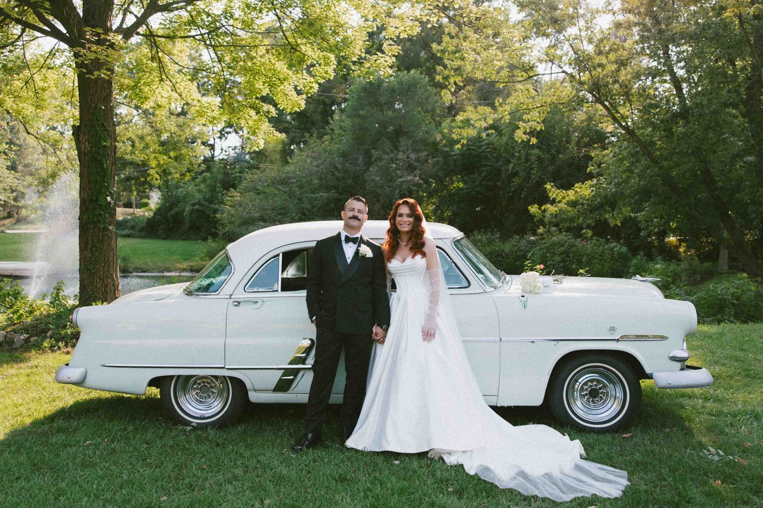 A classic white vintage car serves as backdrop for a wedding photo.