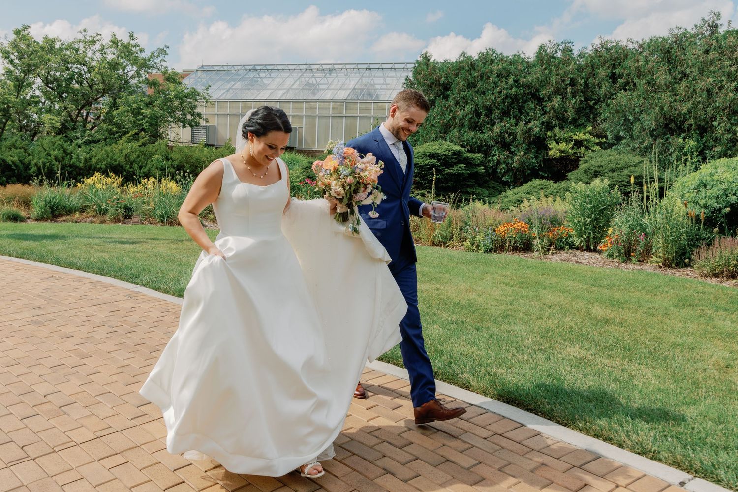 Couple in wedding attire dancing and twirling on outdoor brick patio.