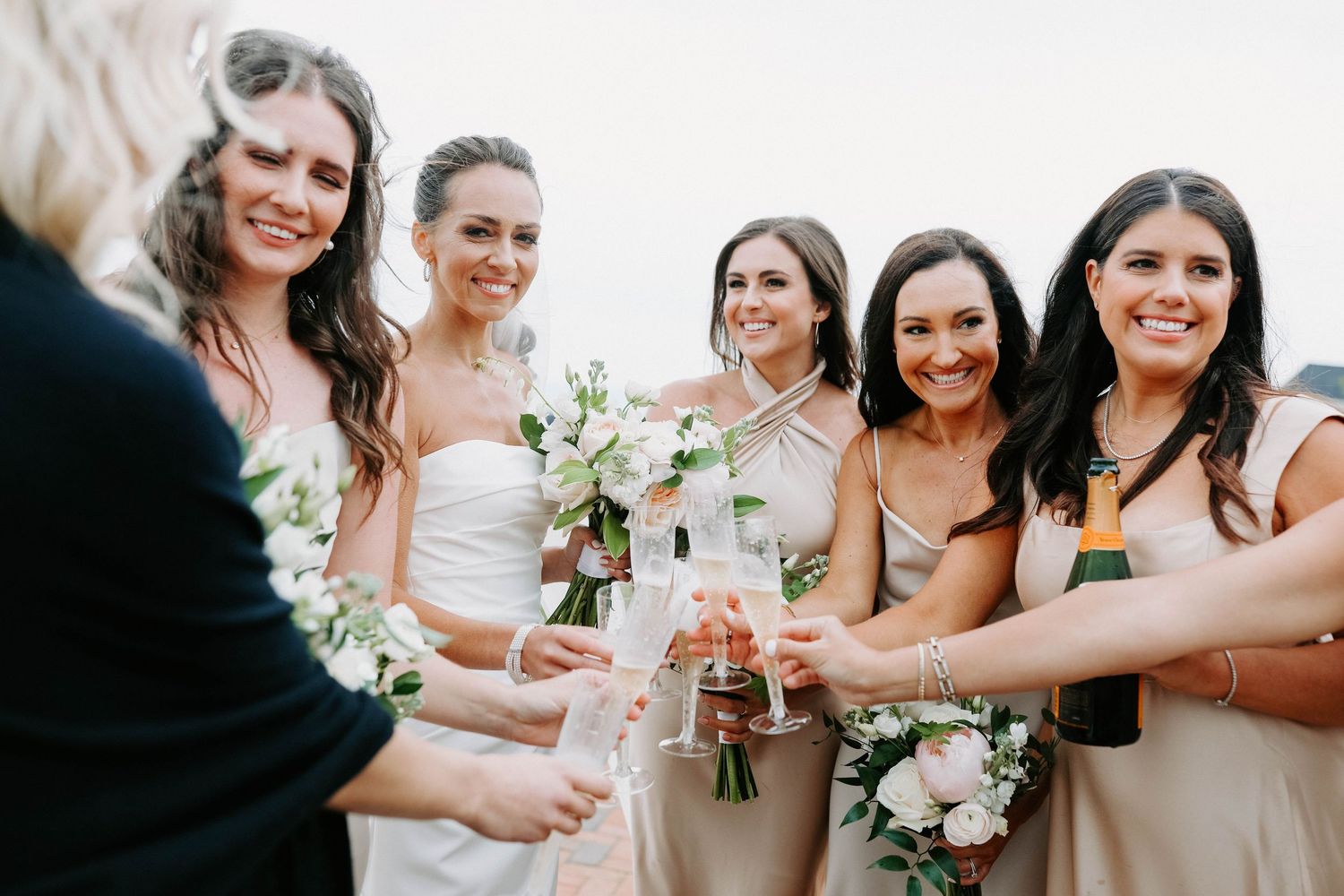 Wedding party toasts with champagne while holding floral bouquets.