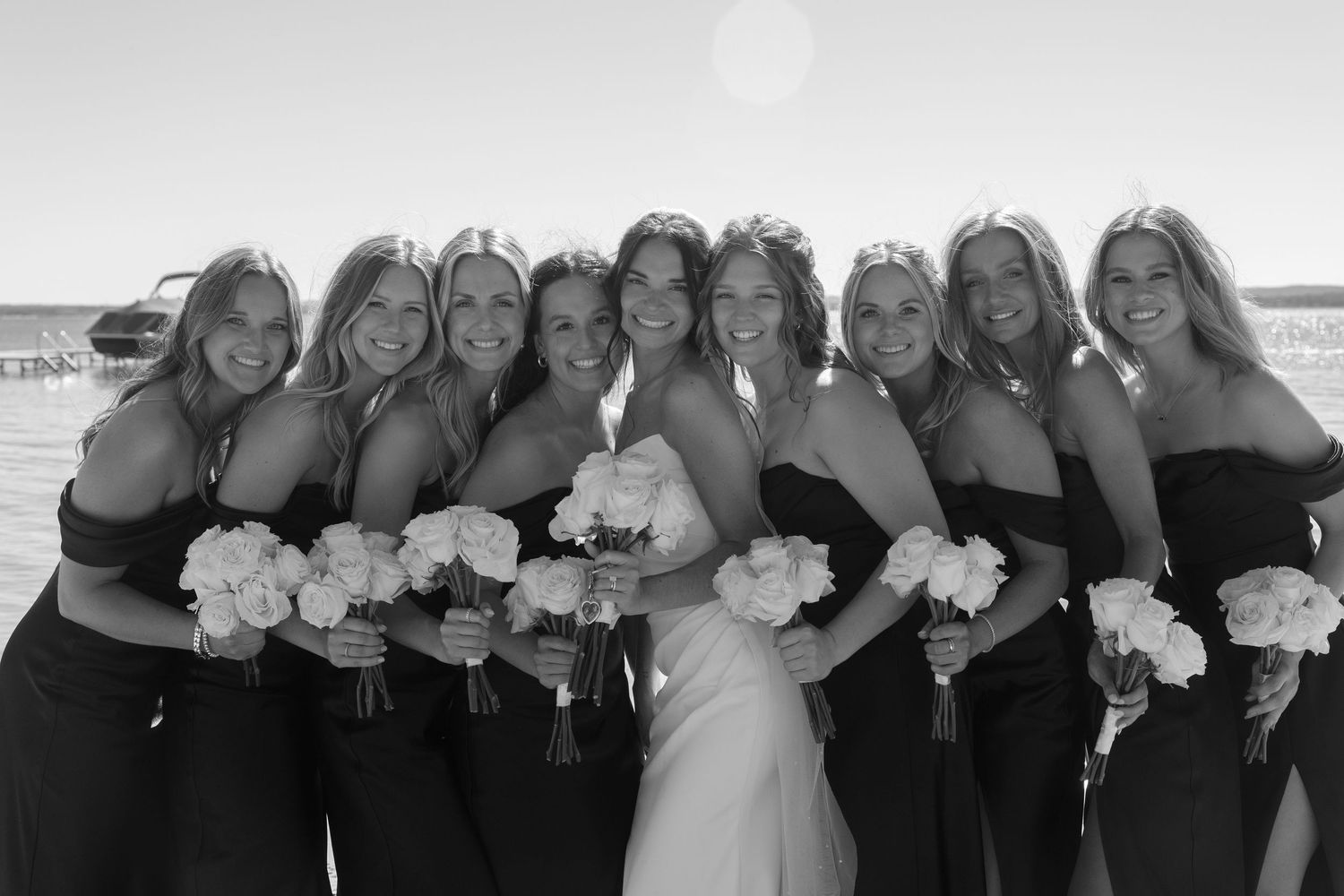 Bridesmaids in matching dresses pose together holding white bouquets on the beach.