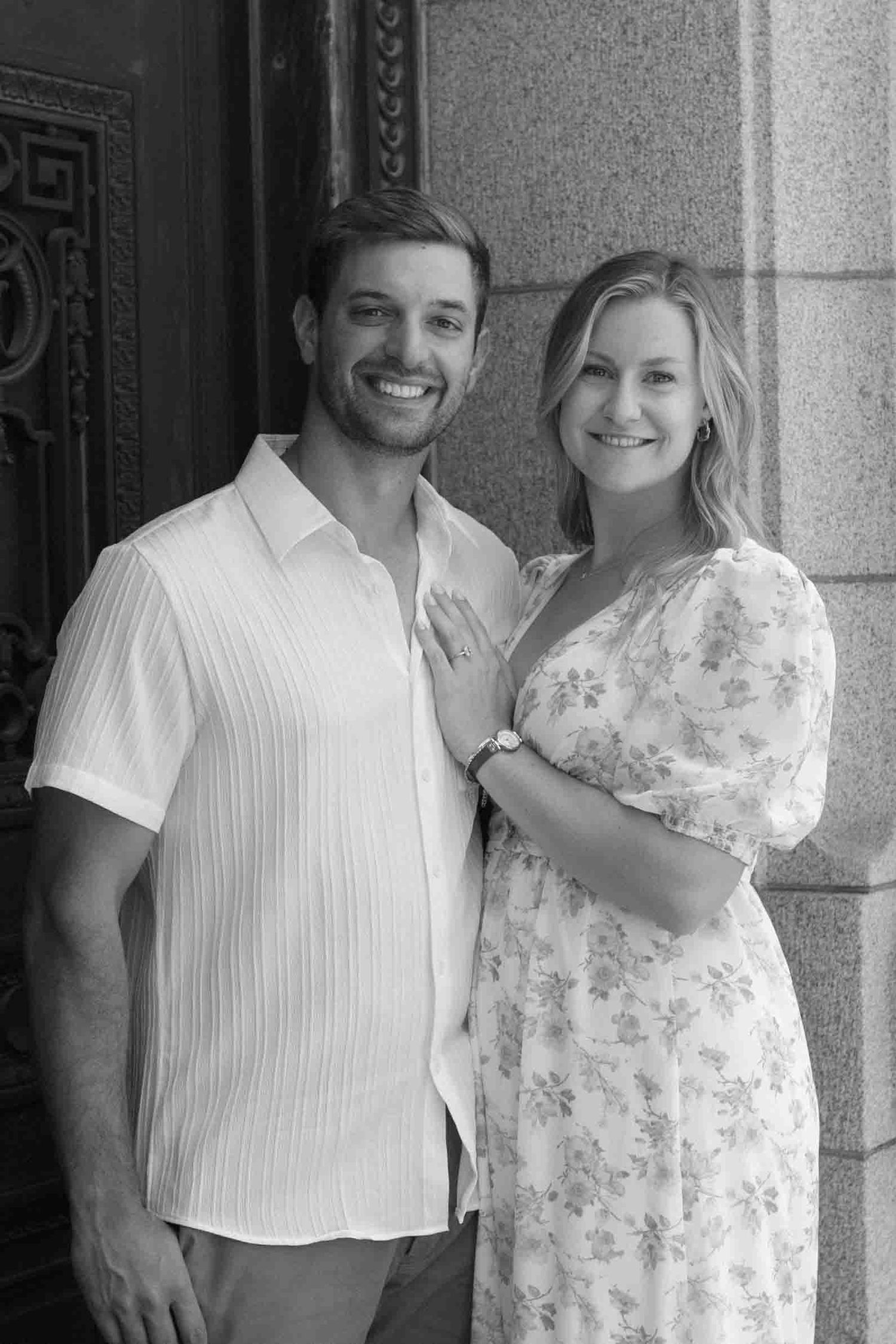 A couple poses together against a stone building wearing coordinated white outfits.