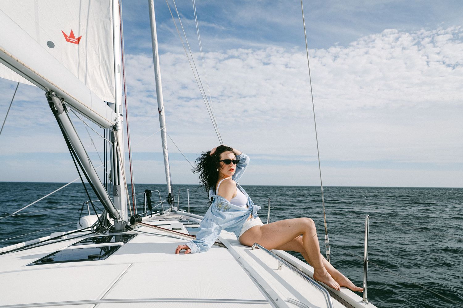 A person relaxes on a sailboat deck while cruising across blue ocean waters on a sunny summer day.
