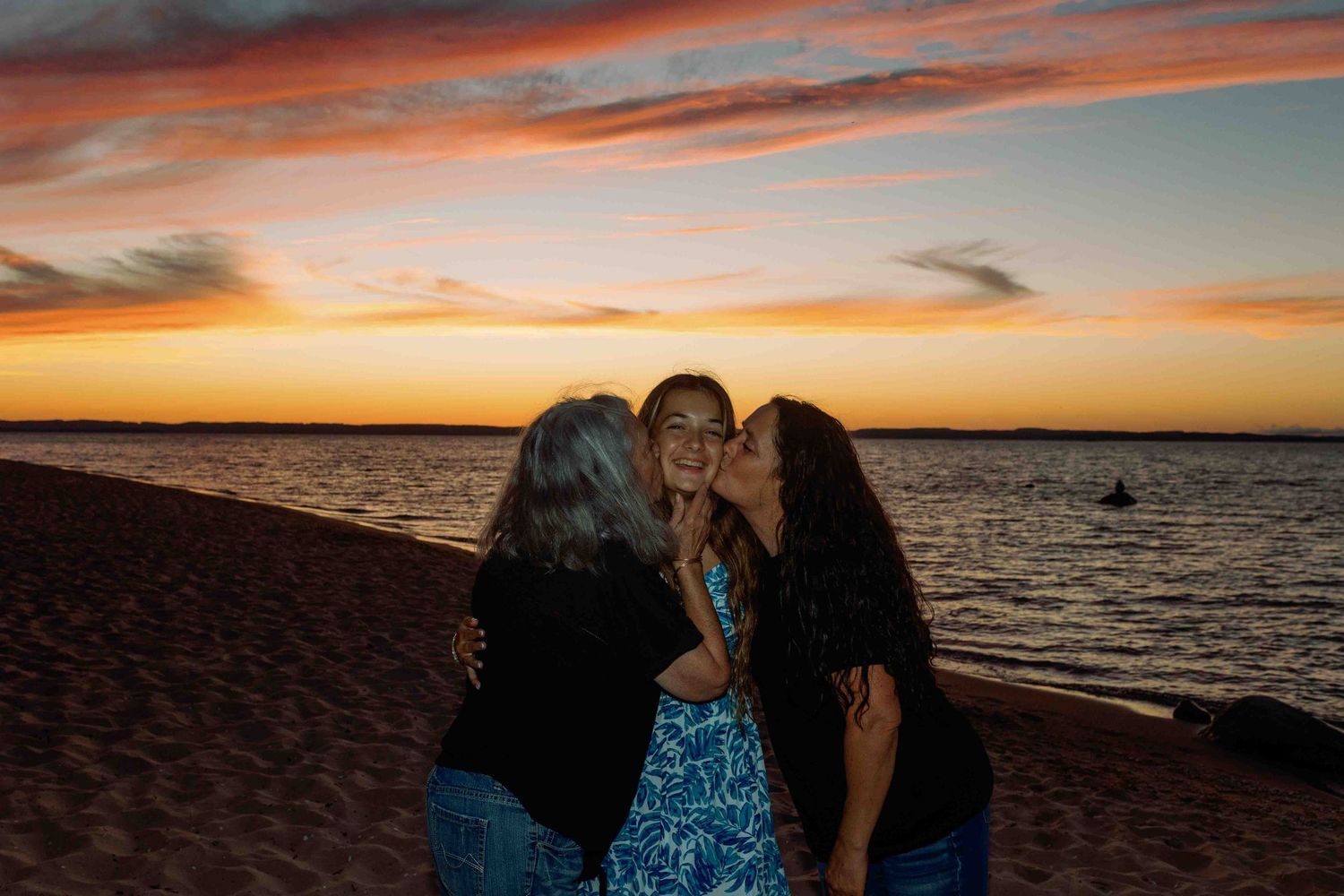 Friends gathering on a beach at sunset with orange sky reflecting on the water.
