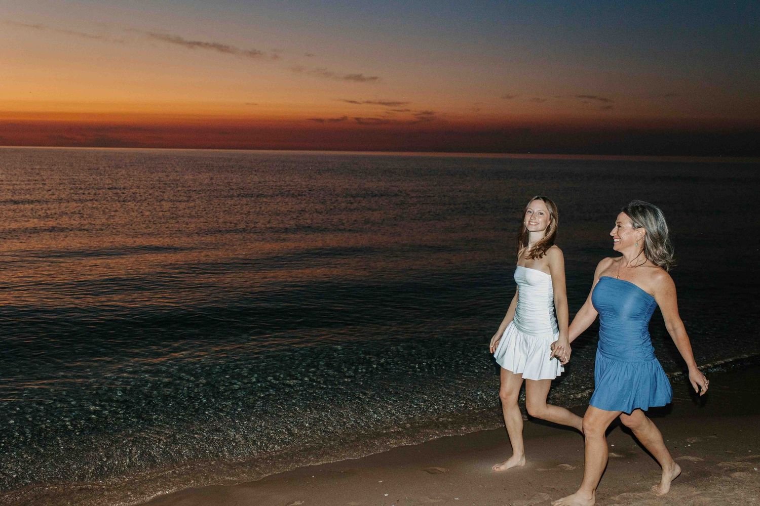 People walking along beach shore during golden hour sunset.