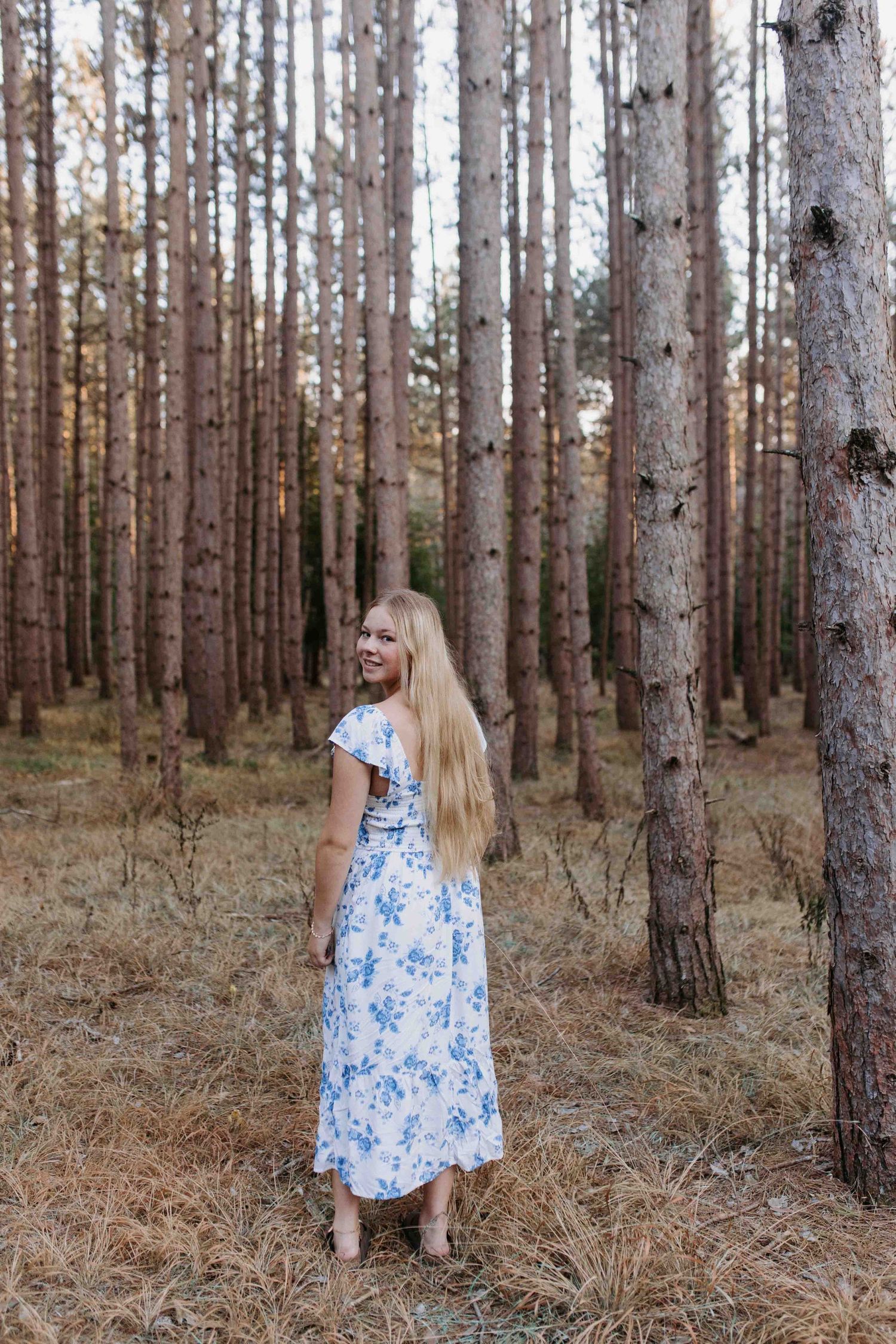 Long floral dress photographed in a pine forest with natural lighting.