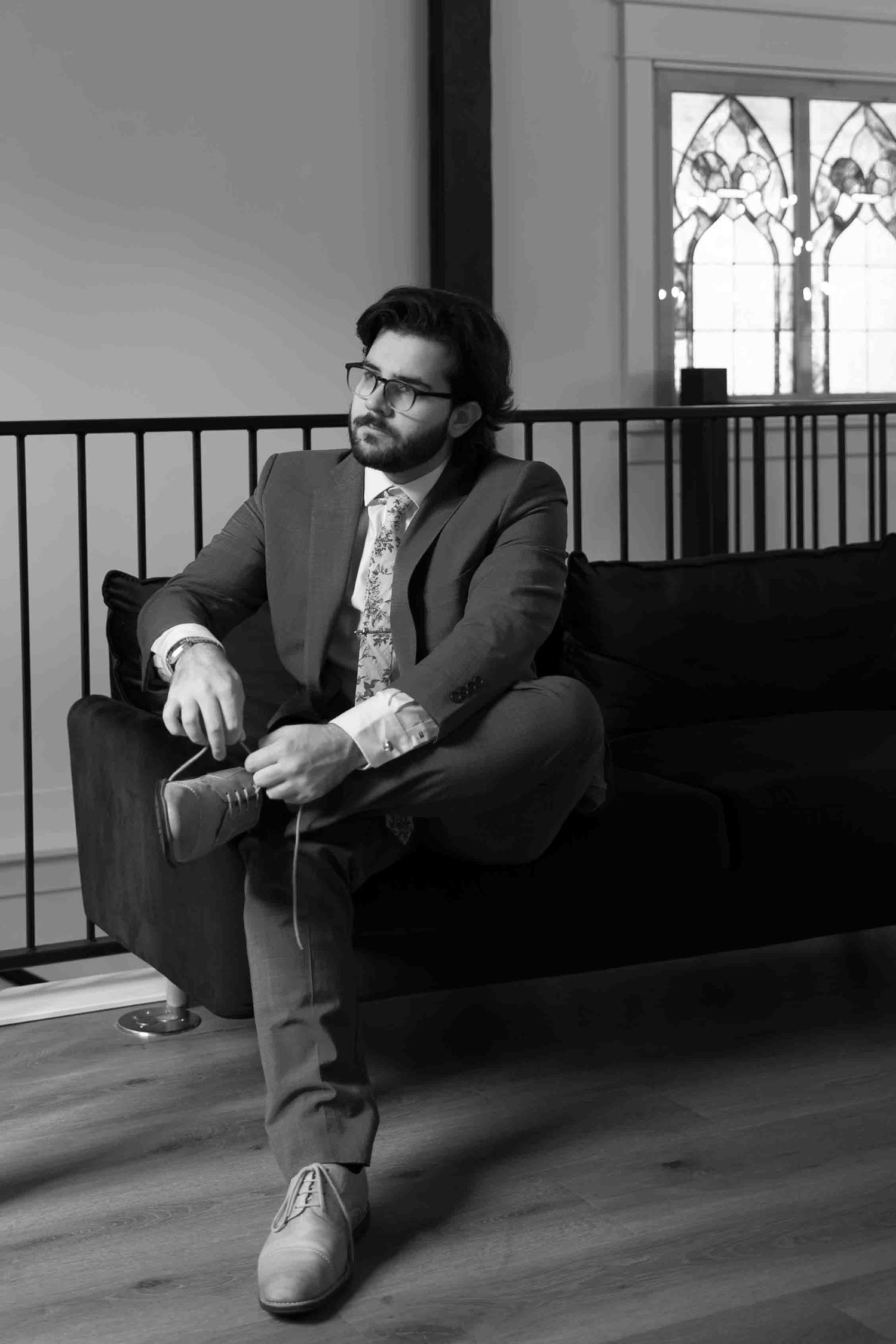Person in dark suit sitting casually on wooden floor near window.