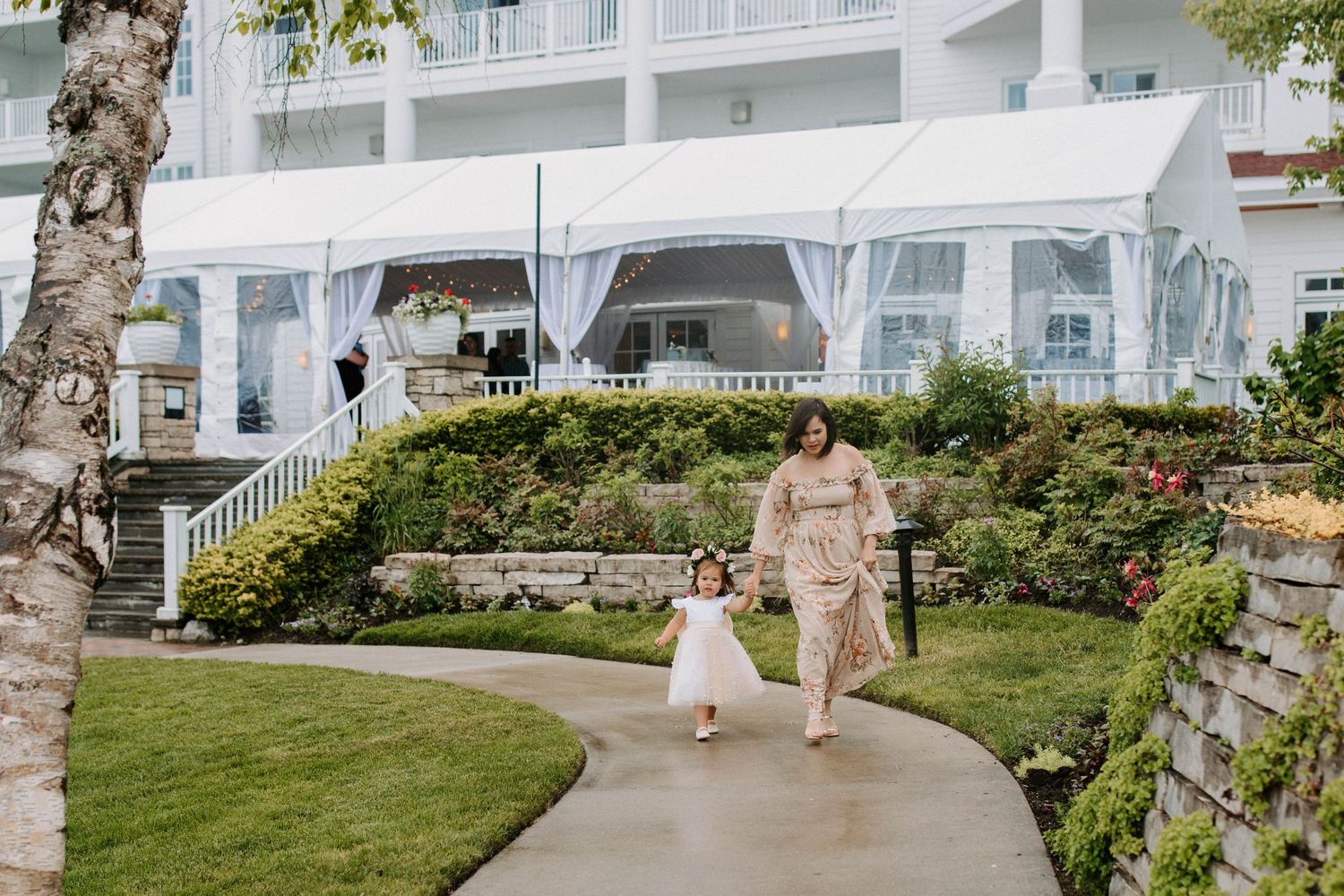 Elegant wedding procession walking along a curved pathway at a waterfront resort.