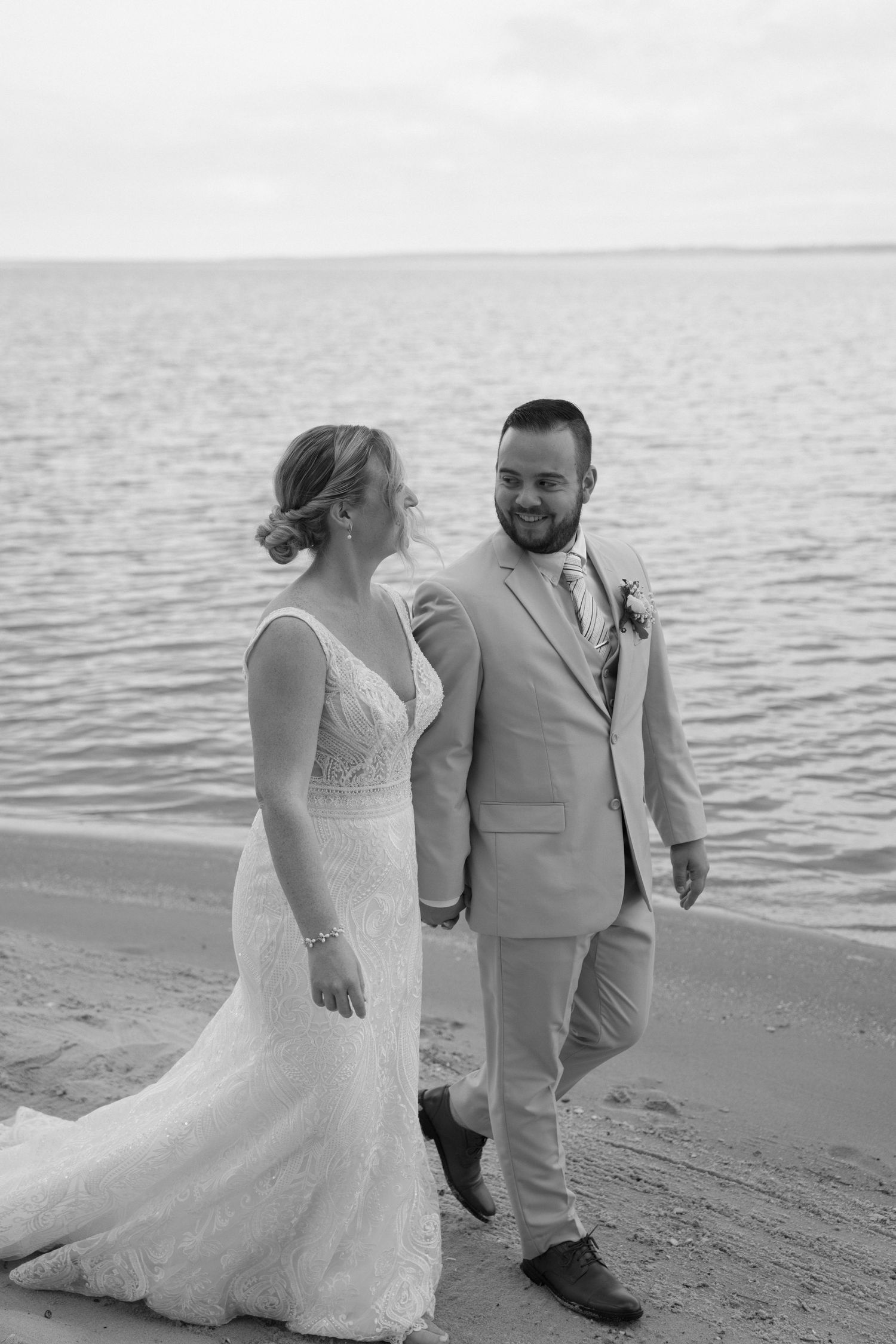 Black and white photos of couple walking along shoreline in wedding attire.