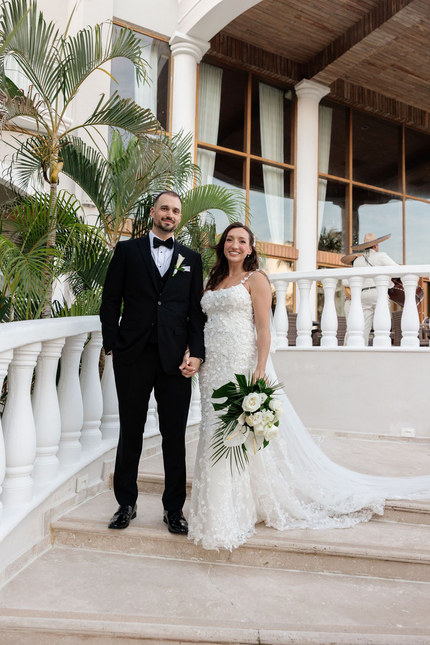 Wedding couple posing on tropical veranda with white columns and palm trees.