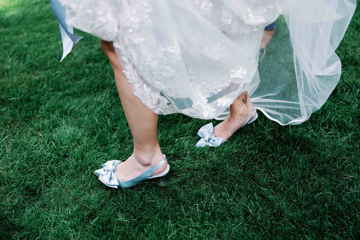 Close-up details of a white wedding dress flowing over green grass.