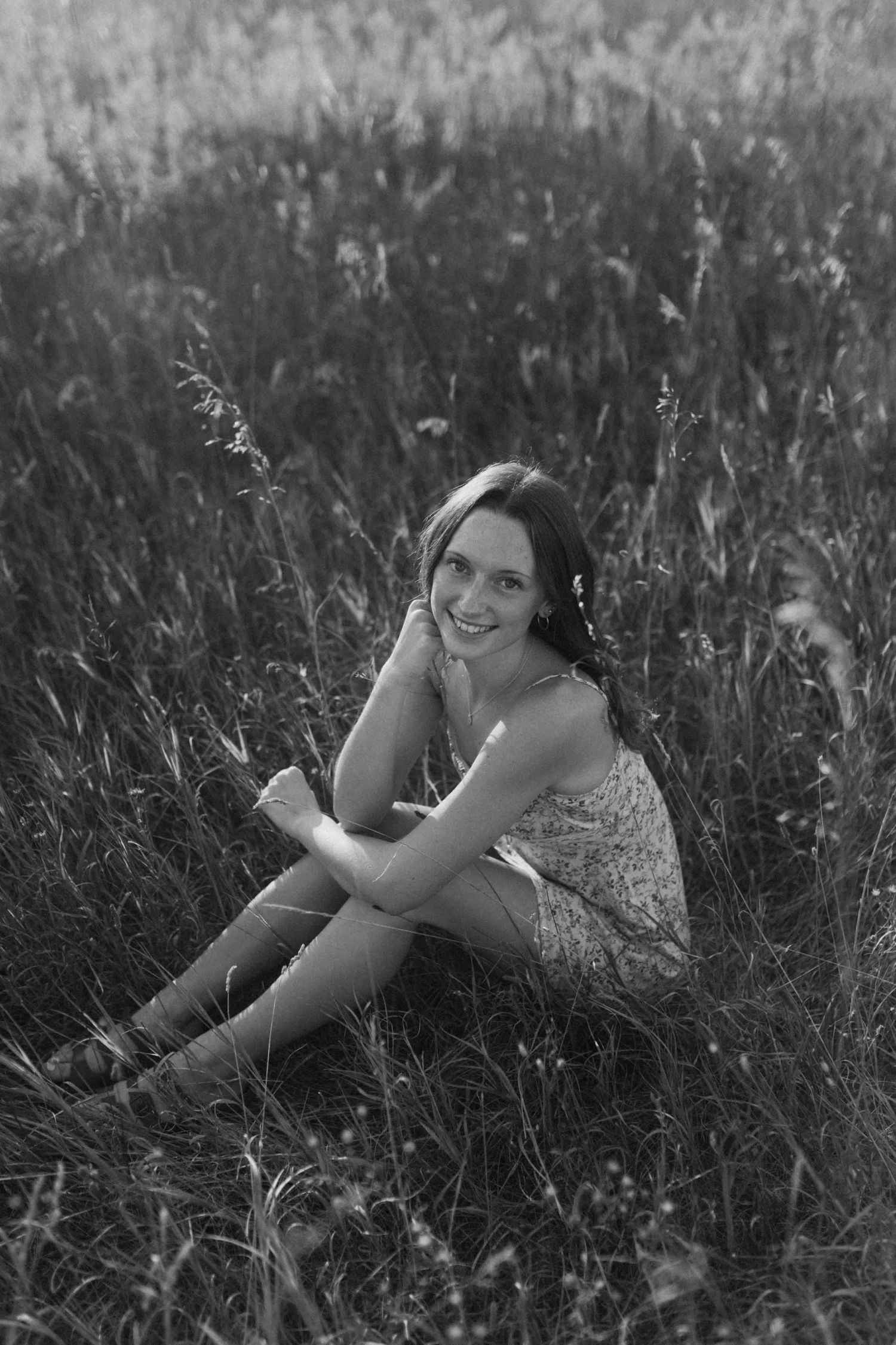 Black and white portrait of someone reclining in a wild grass meadow.