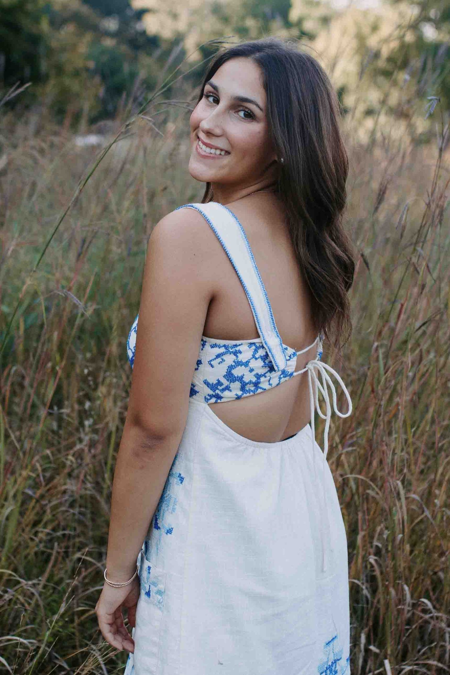 A white and blue patterned sundress photographed in a field of tall grass during golden hour.